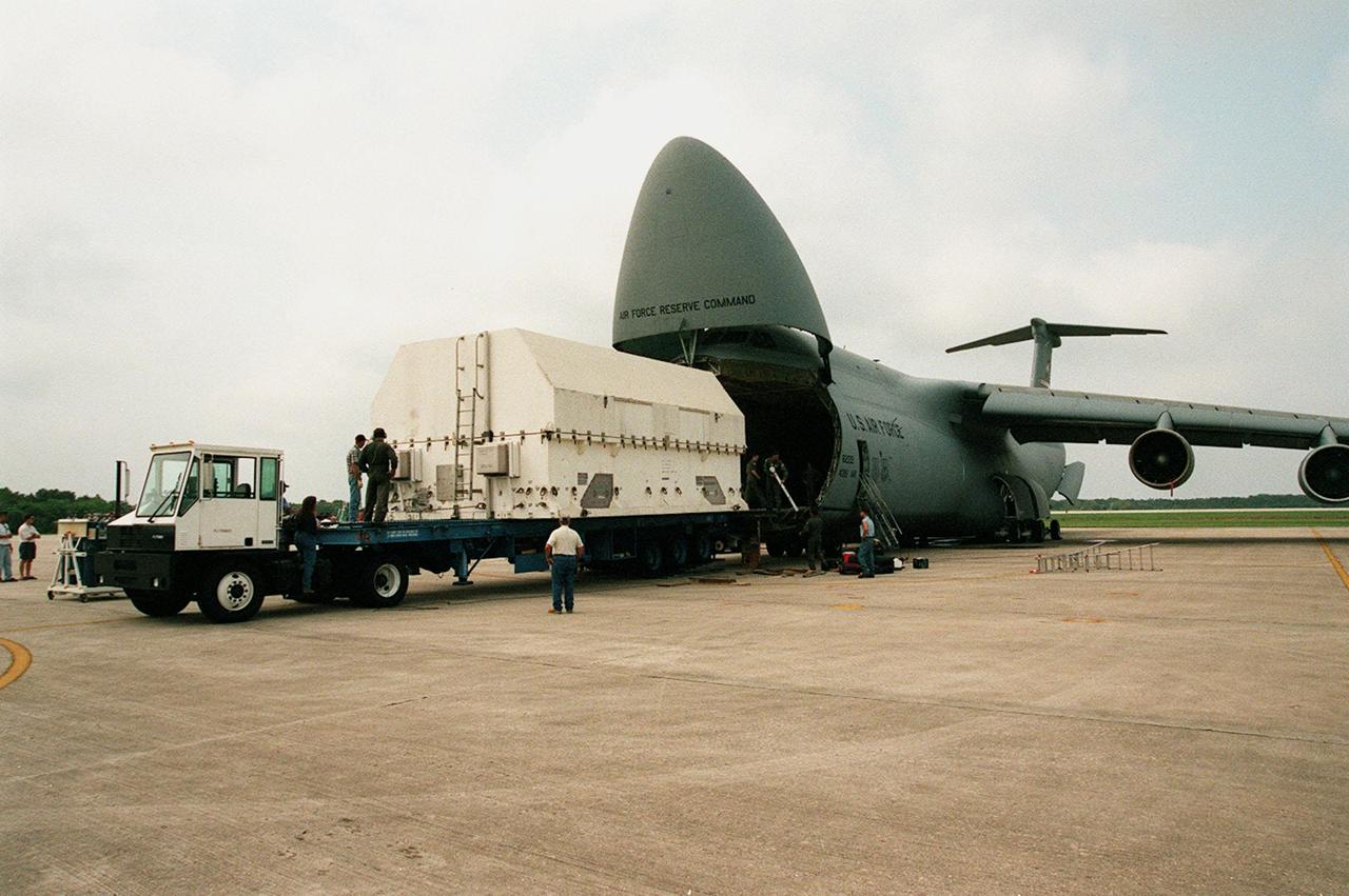 A shipping container with payload flight hardware for the Third Hubble Space Telescope Servicing Mission (SM-3A) is transferred onto a transporter from the C-5 air cargo plane that brought it to KSC. The hardware will be taken to the Payload Hazardous Servicing Facility for final testing and integration of payload elements. Mission STS-103 is a "call-up" mission which is being planned due to the need to replace portions of the Hubble's pointing system, the gyros, which have begun to fail. Although Hubble is operating normally and conducting its scientific observations, only three of its six gyroscopes are working properly. The gyroscopes allow the telescope to point at stars, galaxies and planets. The STS-103 crew will not only replace gyroscopes, it will also replace a Fine Guidance Sensor and an older computer with a new enhanced model, an older data tape recorder with a solid state digital recorder, a failed spare transmitter with a new one, and degraded insulation on the telescope with new thermal insulation. The crew will also install a Battery Voltage/Temperature Improvement Kit to protect the spacecraft batteries from overcharging and overheating when the telescope goes into a safe mode. Launch of STS-93 is currently targeted for Oct. 14 but under review, pending the launch date of a prior mission, STS-99, also under review