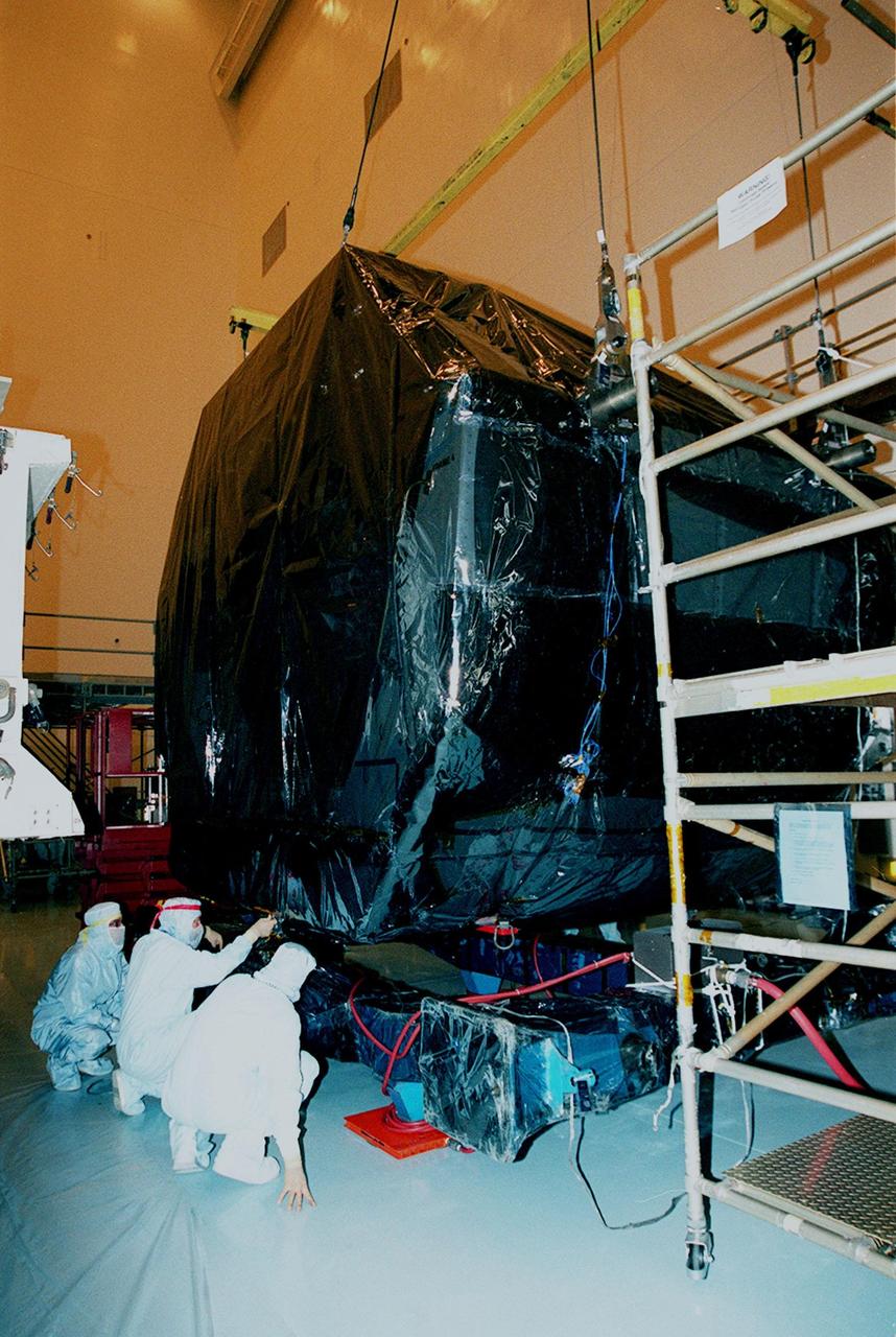 In the Payload Hazardous Servicing Facility (PHSF), workers check the placement of equipment, part of mission STS-103, onto a workstand. The equipment is the first part of payload flight hardware for the third Hubble Space Telescope Servicing Mission (SM-3A). The hardware will undergo final testing and integration of payload elements in the PHSF. Mission STS-103 is a "call-up" mission which is being planned due to the need to replace portions of the Hubble's pointing system, the gyros, which have begun to fail. Although Hubble is operating normally and conducting its scientific observations, only three of its six gyroscopes are working properly. The gyroscopes allow the telescope to point at stars, galaxies and planets. The STS-103 crew will not only replace gyroscopes, it will also replace a Fine Guidance Sensor and an older computer with a new enhanced model, an older data tape recorder with a solid state digital recorder, a failed spare transmitter with a new one, and degraded insulation on the telescope with new thermal insulation. The crew will also install a Battery Voltage/Temperature Improvement Kit to protect the spacecraft batteries from overcharging and overheating when the telescope goes into a safe mode. Launch of STS-103 is currently targeted for Oct. 14 but the date is under review