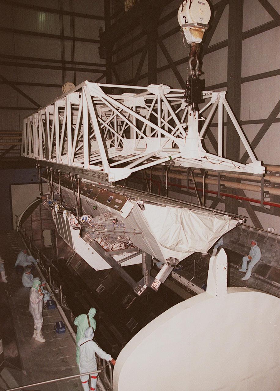In the Orbiter Processing Facility, workers observe as an overhead crane lowers the Shuttle Radar Topography Mission (SRTM) into a payload canister. The payload on mission STS-99, SRTM was removed from orbiter Endeavour's payload bay to allow technicians access to the orbiter's midbody for planned wiring inspections. The entire fleet of orbiters is being inspected for wiring abrasions after the problem was first discovered in Columbia. Shuttle managers are reviewing several manifest options and could establish new target launch dates for the balance of 1999 next week. Shuttle Endeavour currently remains slated for launch in early October