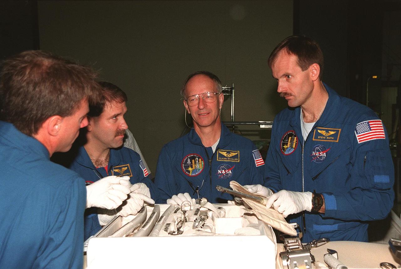 In the Orbiter Processing Facility (OPF) bay 1, STS-103 crew members look over equipment to be used on planned Extravehicular Activities (EVAs) on the mission for repair of the Hubble Space Telescope. They are taking part in a Crew Equipment Interface Test (CEIT) at KSC. From left are Mission Specialists C. Michael Foale (Ph.D.), John M. Grunsfeld (Ph.D.) Claude Nicollier of Switzerland, and Steven L. Smith. Other crew members at KSC for the CEIT are Commander Curtis L. Brown Jr., Pilot Scott J. Kelly, and Jean-François Clervoy of France. Nicollier and Clervoy are with the European Space Agency. Mission STS-103 is a "call-up" due to the need to replace portions of the pointing system, the gyros, which have begun to fail on the Hubble Space Telescope. Although Hubble is operating normally and conducting its scientific observations, only three of its six gyroscopes are working properly. The gyroscopes allow the telescope to point at stars, galaxies and planets. The STS-103 crew will not only replace gyroscopes, it will also replace a Fine Guidance Sensor and an older computer with a new enhanced model, an older data tape recorder with a solid-state digital recorder, a failed spare transmitter with a new one, and degraded insulation on the telescope with new thermal insulation. The crew will also install a Battery Voltage/Temperature Improvement Kit to protect the spacecraft batteries from overcharging and overheating when the telescope goes into a safe mode. The scheduled launch date in October is under review