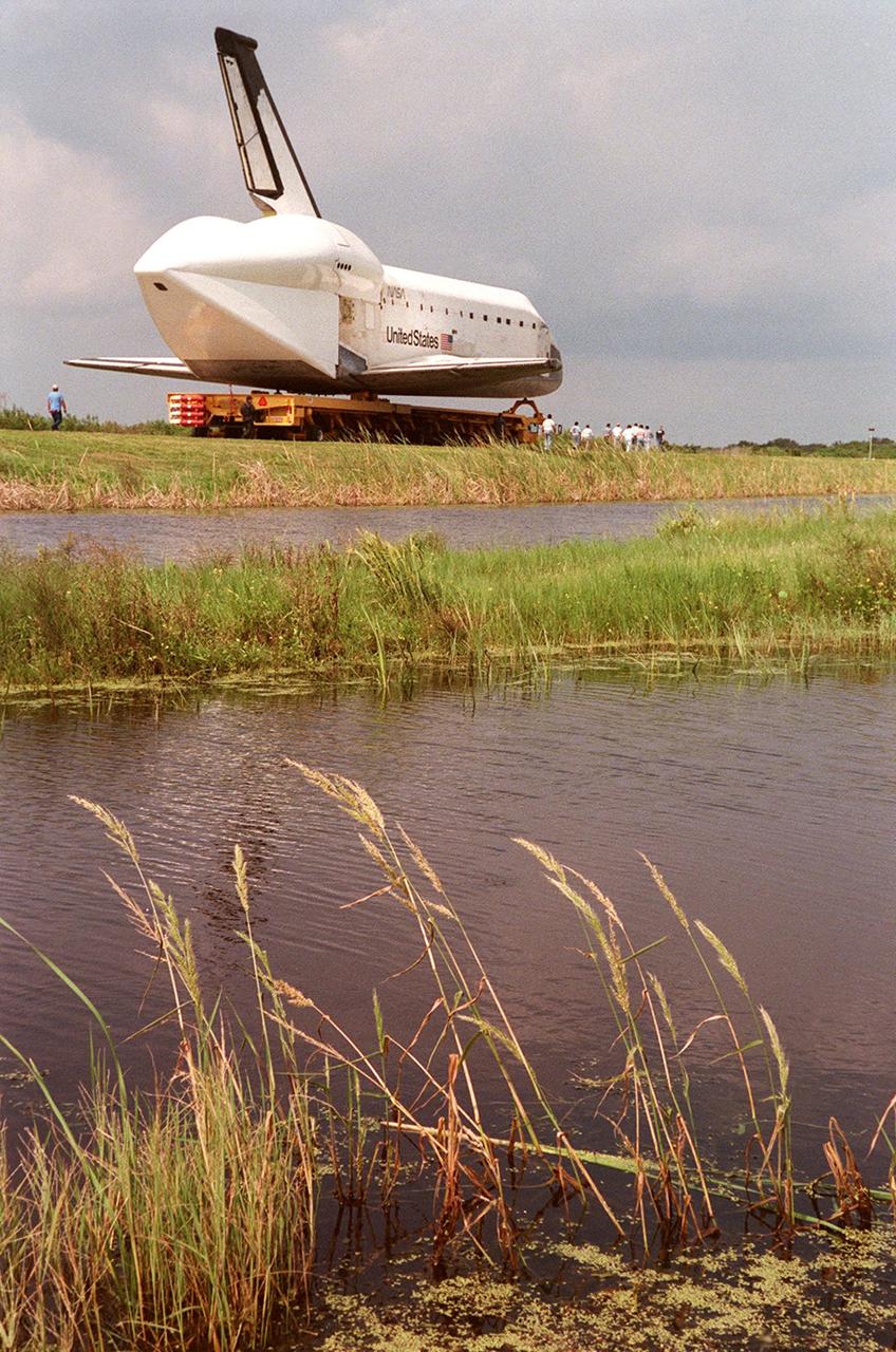 KENNEDY SPACE CENTER, FLA. -- Aboard a transporter, the orbiter Columbia is moved on the tow-way along the Banana Creek. Columbia is heading to the Shuttle Landing Facility's (SLF) Mate-Demate Device where it will be mated to the Boeing 747 Shuttle Carrier Aircraft for a ferry flight to Palmdale, Calif. On the rear of the orbiter can be seen the tail cone, a fairing that is installed over the aft fuselage of the orbiter to decrease aerodynamic drag and buffet when the Shuttle Carrier Aircraft is transporting the orbiter cross-country. It is 36 feet long, 25 feet wide, and 22 feet high. Columbia, the oldest of four orbiters in NASA's fleet, will undergo extensive inspections and modifications in Boeing's Orbiter Assembly Facility during a nine-month orbiter maintenance down period (OMDP), the second in its history. Orbiters are periodically removed from flight operations for an OMDP. Columbia's first was in 1994. Along with more than 100 modifications on the vehicle, Columbia will be the second orbiter to be outfitted with the multifunctional electronic display system, or "glass cockpit." Columbia is expected to return to KSC in July 2000