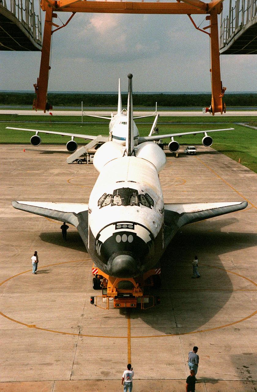 KENNEDY SPACE CENTER, FLA. -- The orbiter Columbia (foreground) moves under the Mate-Demate Device at KSC's Shuttle Landing Facility (SLF). The crane seen above it will lift the orbiter so that the Boeing 747 Shuttle Carrier Aircraft (SCA) in the background can move underneath Columbia, which will then be attached to the back of the SCA for a ferry flight to Palmdale, Calif. On the rear of the orbiter is the tail cone, a fairing that is installed over the aft fuselage of the orbiter to decrease aerodynamic drag and buffet when the Shuttle Carrier Aircraft is transporting the orbiter cross-country. It is 36 feet long, 25 feet wide, and 22 feet high. Columbia, the oldest of four orbiters in NASA's fleet, will undergo extensive inspections and modifications in Boeing's Orbiter Assembly Facility during a nine-month orbiter maintenance down period (OMDP), the second in its history. Orbiters are periodically removed from flight operations for an OMDP. Columbia's first was in 1994. Along with more than 100 modifications on the vehicle, Columbia will be the second orbiter to be outfitted with the multifunctional electronic display system, or "glass cockpit." Columbia is expected to return to KSC in July 2000