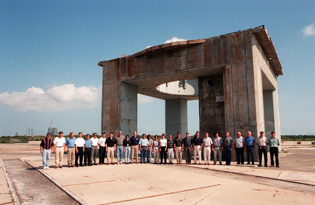 At Cape Canaveral Air Station, members of the 1998 astronaut candidate class (Group 17) pose in front of what remains of the launch tower at Launch Complex 34 during a tour of the station's facilities. During the Apollo Program, Launch Complex 34 was the site of the first Saturn I and Saturn IB launches, as well as the tragic fire in which the Apollo I astronauts lost their lives. The class is at Kennedy Space Center taking part in training activities, including a flight awareness program, as well as touring the OPF, VAB, SSPF, SSME Processing Facility, launch pads, SLF, Apollo/Saturn V Center, and the crew quarters. The U.S. candidates in the '98 class are Clayton C. Anderson, Lee J. Archambault, Tracy E. Caldwell (Ph.D.), Gregory E. Chamitoff (Ph.D.), Timothy J. Creamer, Christopher J. Ferguson, Michael J. Foreman, Michael E. Fossum, Kenneth T. Ham, Patricia C. Hilliard (M.D.), Gregory C. Johnson, Gregory H. Johnson, Stanley G. Love (Ph.D.), Leland D. Melvin, Barbara R. Morgan, William A. Oefelein, John D. Olivas (Ph.D.), Nicholas J.M. Patrick (Ph.D.), Alan G. Poindexter, Garrett E. Reisman (Ph.D.), Steven R. Swanson, Douglas H. Wheelock, Sunita L. Williams, Neil W. Woodward III, George D. Zamka; and the international candidates are Leopold Eyharts, Paolo Nespoli, Hans Schlegel, Roberto Vittori, Bjarni V. Tryggvason, and Marcos Pontes