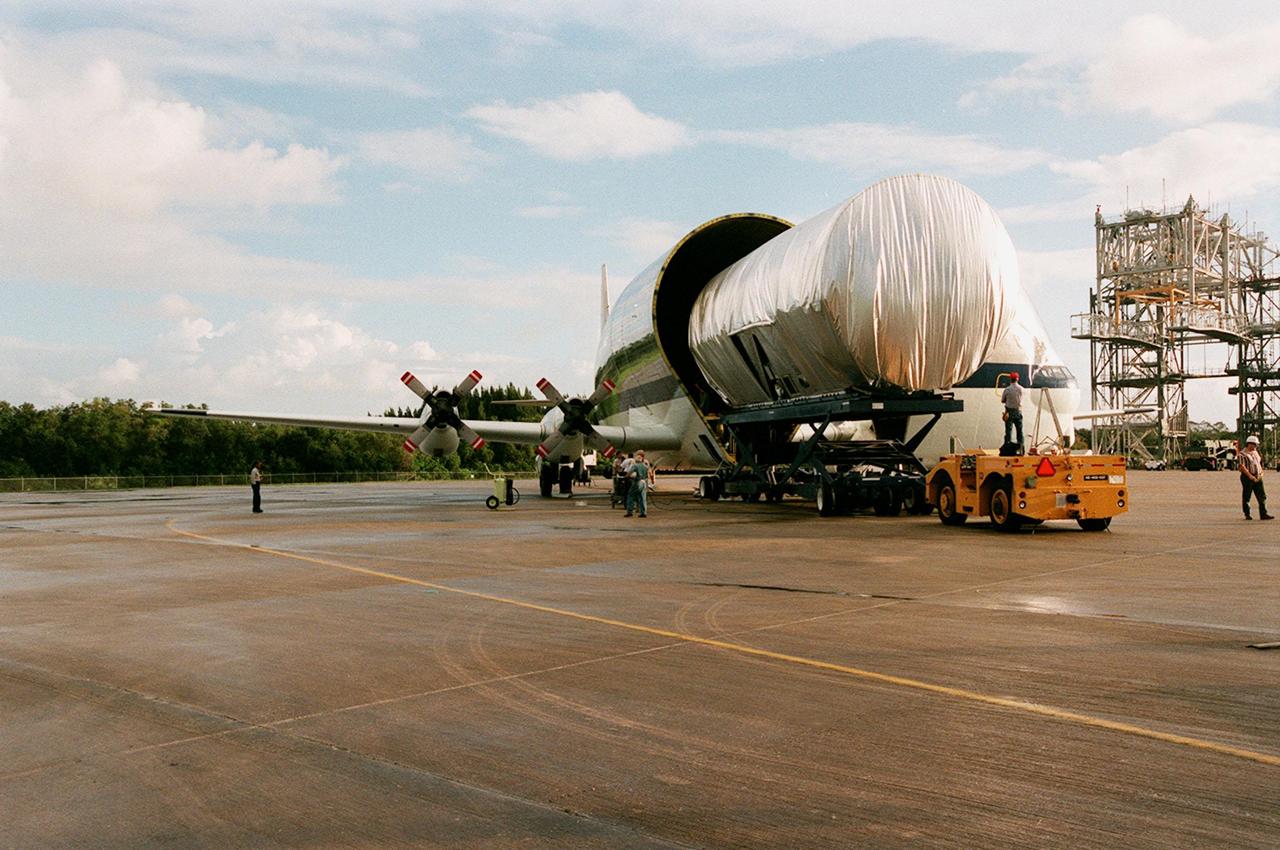 KENNEDY SPACE CENTER, FLA. -- At the Shuttle Landing Facility, the newly arrived S1 truss, a segment of the International Space Station (ISS), is offloaded from NASA's Super Guppy aircraft. Manufactured by the Boeing Co. in Huntington Beach, Calif., this component of the ISS is the first starboard (right-side) truss segment, whose main job is providing structural support for the orbiting research facility's radiator panels that cool the Space Station's complex power system. The S1 truss segment also will house communications systems, external experiment positions and other subsystems. Primarily constructed of aluminum, the truss segment is 45 feet long, 15 feet wide and 6 feet tall. When fully outfitted, it will weigh 31,137 pounds. The truss is slated for flight in 2001. The Super Guppy, with its 25-foot diameter fuselage designed to handle oversized loads, is well prepared to transport the truss and other ISS segments. Loading the Guppy is easy because of the unique "fold-away" nose of the aircraft that opens 110 degrees for cargo loading. A system of rails in the cargo compartment, used with either Guppy pallets or fixtures designed for specific cargo, makes cargo loading simple and efficient. Rollers mounted in the rails allow pallets or fixtures to be moved by an electric winch mounted beneath the cargo floor. Automatic hydraulic lock pins in each rail secure the pallet for flight. The truss is being transferred to the Operations and Checkout Building
