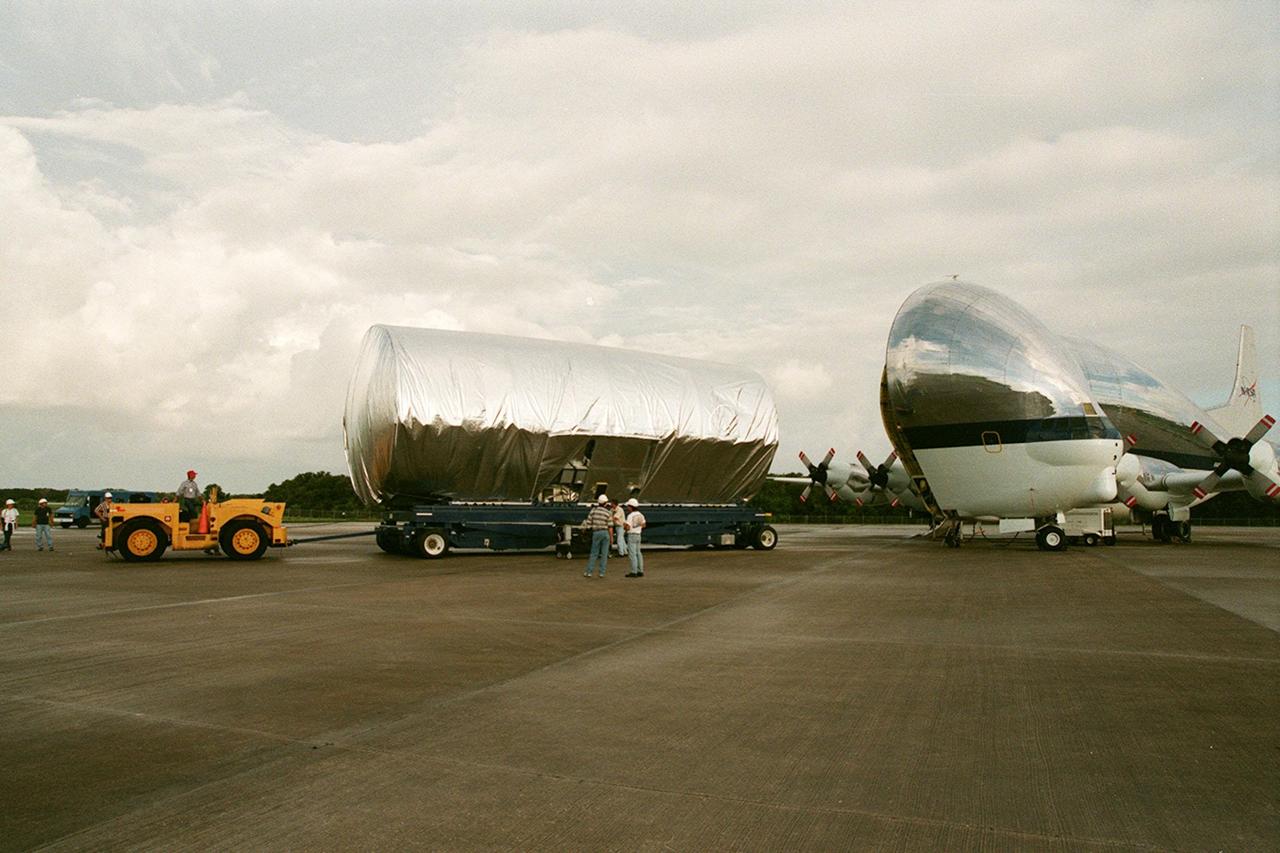 KENNEDY SPACE CENTER, FLA. -- At the Shuttle Landing Facility, the S1 truss, a segment of the International Space Station, is moved away from the Super Guppy that brought it to KSC from Marshall Space Flight Center. Manufactured by the Boeing Co. in Huntington Beach, Calif., this component of the ISS is the first starboard (right-side) truss segment, whose main job is providing structural support for the orbiting research facility's radiator panels that cool the Space Station's complex power system. The S1 truss segment also will house communications systems, external experiment positions and other subsystems. Primarily constructed of aluminum, the truss segment is 45 feet long, 15 feet wide and 6 feet tall. When fully outfitted, it will weigh 31,137 pounds. The truss is slated for flight in 2001. The Super Guppy, with its 25-foot diameter fuselage designed to handle oversized loads, is well prepared to transport the truss and other ISS segments. Loading the Guppy is easy because of the unique "fold-away" nose of the aircraft that opens 110 degrees for cargo loading. A system of rails in the cargo compartment, used with either Guppy pallets or fixtures designed for specific cargo, makes cargo loading simple and efficient. Rollers mounted in the rails allow pallets or fixtures to be moved by an electric winch mounted beneath the cargo floor. Automatic hydraulic lock pins in each rail secure the pallet for flight. The truss is being transferred to the Operations and Checkout Building