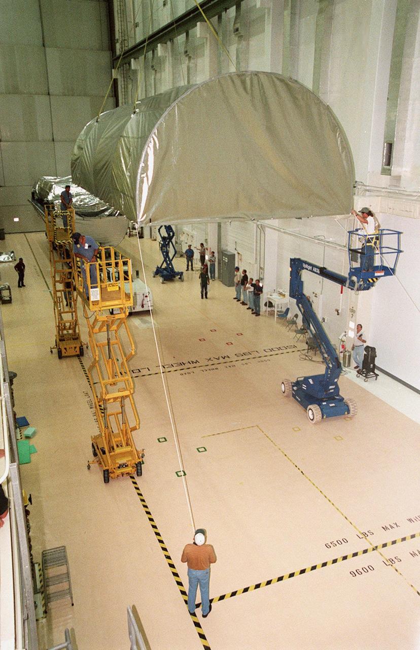 KENNEDY SPACE CENTER, FLA. -- Inside the Operations and Checkout Building, the top of the Guppy cargo carrier is lifted off the S1 truss (background). Manufactured by the Boeing Co. in Huntington Beach, Calif., this component of the International Space Station is the first starboard (right-side) truss segment, whose main job is providing structural support for the orbiting research facility's radiator panels that cool the Space Station's complex power system. The S1 truss segment also will house communications systems, external experiment positions and other subsystems. Primarily constructed of aluminum, the truss segment is 45 feet long, 15 feet wide and 6 feet tall. When fully outfitted, it will weigh 31,137 pounds. The truss is slated for flight in 2001