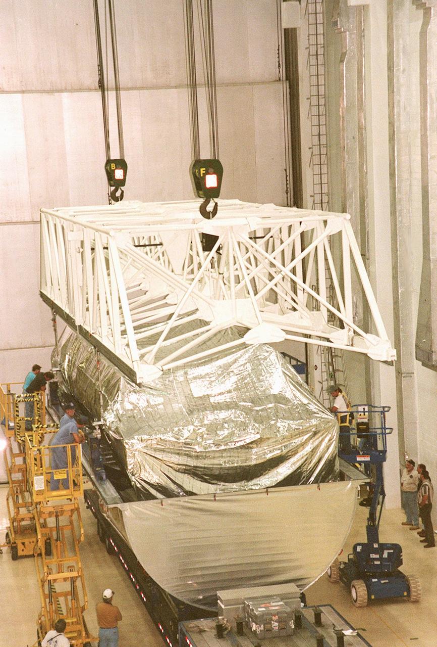 KENNEDY SPACE CENTER, FLA. -- Inside the Operations and Checkout Building, a strongback is lowered toward the S1 truss below it in order to lift the truss from the Guppy cargo carrier that protected it during flight and transfer. Manufactured by the Boeing Co. in Huntington Beach, Calif., this component of the International Space Station is the first starboard (right-side) truss segment, whose main job is providing structural support for the orbiting research facility's radiator panels that cool the Space Station's complex power system. The S1 truss segment also will house communications systems, external experiment positions and other subsystems. Primarily constructed of aluminum, the truss segment is 45 feet long, 15 feet wide and 6 feet tall. When fully outfitted, it will weigh 31,137 pounds. The truss is slated for flight in 2001
