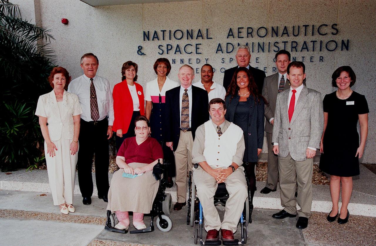 Center Director Roy Bridges (standing, center) poses with members of the Disability Awareness and Action Working Group (DAAWG), which is holding the 1999 Technology Fair Oct. 20-21 at Kennedy Space Center. The Fair is highlighting vendors demonstrating mobility, hearing, vision and silent disability assistive technology. The purpose is to create an awareness of the types of technology currently available to assist people with various disabilities in the workplace. The theme is that of this year's National Disability Employment Awareness Month, "Opening Doors to Ability." Some of the vendors participating are Canine Companions for Independence, Goodwill Industries, Accessible Structures, Division of Blind Services, Space Coast Center for Independent Living, KSC Fitness Center and Delaware North Parks Services