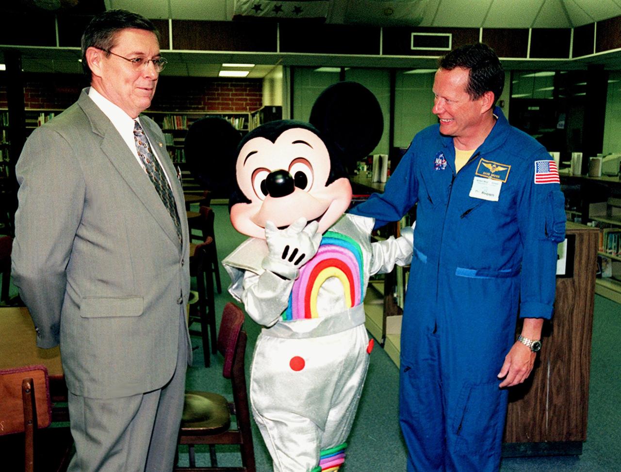 Dr. David Sawyer (left), Superintendent of the Brevard County School District, Mickey Mouse, and Dr. David Brown, a NASA astronaut, attend a tribute to NASA astronaut Ronald McNair held in the gymnasium of Ronald McNair Magnet School in Cocoa, Fla. During the tribute, Walt Disney World presented a portrait of McNair to the school, which had previously been renamed for the fallen astronaut. McNair was one of a crew of seven who lost their lives during an accident following launch of the Space Shuttle Challenger in January 1986