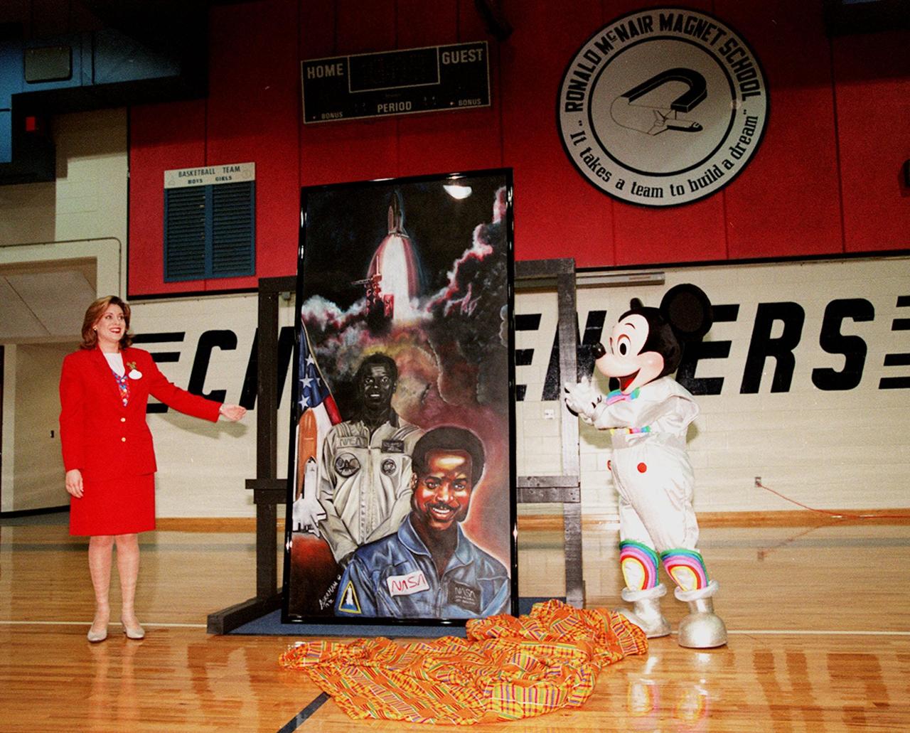 In the gymnasium of Ronald McNair Magnet School in Cocoa, Fla., Ms. Maria Rodriguez, an Walt Disney World Ambassador, and Mickey Mouse pose with a portrait of NASA astronaut Ronald McNair. The portrait was presented to the school by Walt Disney World during a tribute to McNair. The school had previously been renamed for the fallen astronaut, who was one of a crew of seven who lost their lives during an accident following launch of the Space Shuttle Challenger in January 1986