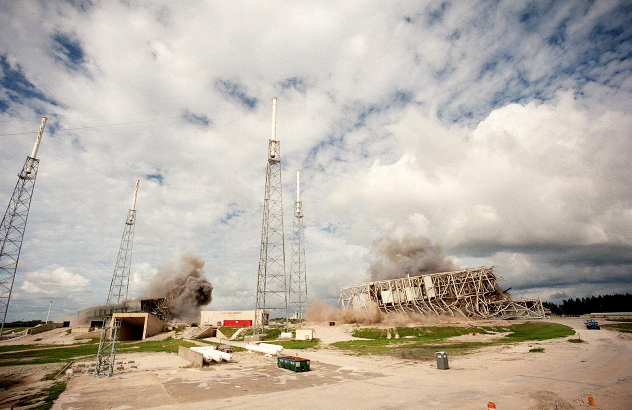KENNEDY SPACE CENTER, FLA. — Two 34-year-old towers on Launch Complex 41, Cape Canaveral Air Station, lie on the ground amid the black smoke from explosives set to topple them. Weighing two million pounds, the umbilical tower (left) was approximately 200 feet high. The taller 300-foot Mobile Service Tower (right) weighs five million pounds. About 200 pounds of linear-shaped charges were used to topple the towers so that the materials can be recycled. Adjacent to the towers are lightning protection structures, which will remain on the site. The towers are being demolished to make room for Lockheed Martin's 14-acre Vehicle Integration Facility (VIF), under construction. The implosion and removal of the tower debris is expected to be completed in two months. The VIF will be used for Lockheed Martin's Atlas V Launch System.