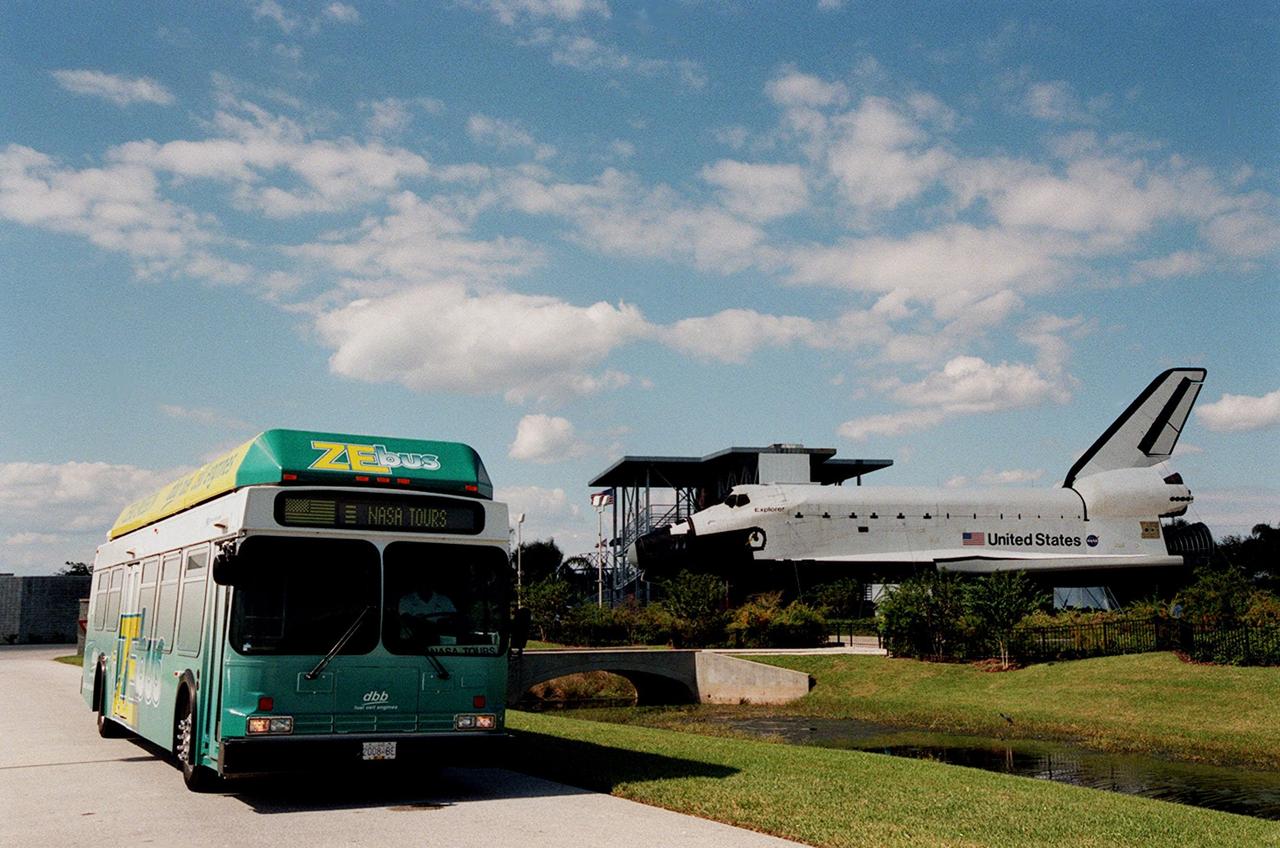 The Zero Emissions (ZE) transit bus passes a mock-up orbiter named Explorer on a trek through the KSC Visitor Complex. Provided by dbb fuel cell engines inc. of Vancouver, Canada, the ZE bus was brought to KSC as part of the Center's Alternative Fuel Initiatives Program. The bus uses a Proton Exchange Membrane fuel cell in which hydrogen and oxygen, from atmospheric air, react to produce electricity that powers an electric motor drive system. The by-product "exhaust" from the fuel cell is water vapor, thus zero harmful emissions. A typical diesel-powered bus emits more than a ton of harmful pollutants from its exhaust every year. The ZE bus is being used on tour routes at the KSC Visitor Complex for two days to introduce the public to the concept