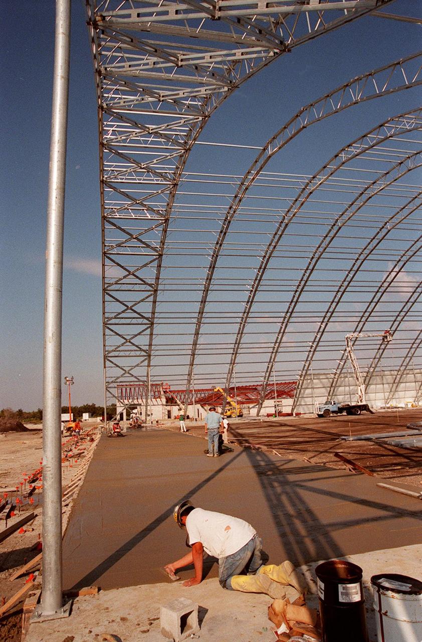 A worker smoothes the recently poured foundation of the multi-purpose hangar at the site of the $8 million Reusable Launch Vehicle (RLV) Support Complex at Kennedy Space Center. In the background can be seen the new construction for the building that will house related ground support equipment and administrative/technical support. The RLV complex will be available to accommodate the Space Shuttle; the X-34 RLV technology demonstrator; the L-1011 carrier aircraft for Pegasus and X-34; and other RLV and X-vehicle programs. The complex is jointly funded by the Spaceport Florida Authority, NASA's Space Shuttle Program and KSC. The facility will be operational in early 2000