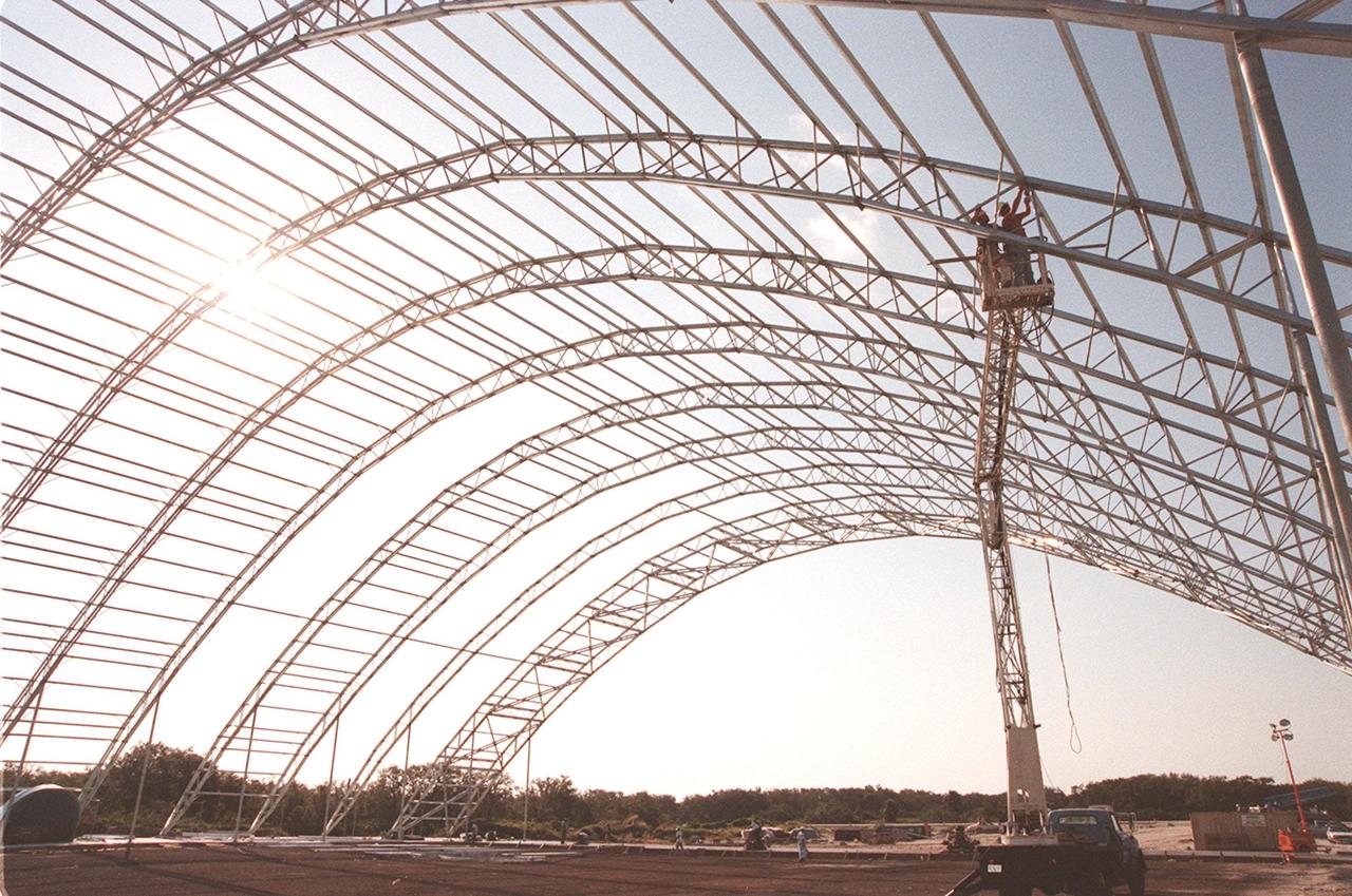 Work continues on the construction of the roof for the multi-purpose hangar at the site of the $8 million Reusable Launch Vehicle (RLV) Support Complex at Kennedy Space Center. In the background can be seen the new construction for the building that will house related ground support equipment and administrative/technical support. The RLV complex will be available to accommodate the Space Shuttle; the X-34 RLV technology demonstrator; the L-1011 carrier aircraft for Pegasus and X-34; and other RLV and X-vehicle programs. The complex is jointly funded by the Spaceport Florida Authority, NASA's Space Shuttle Program and KSC. The facility will be operational in early 2000