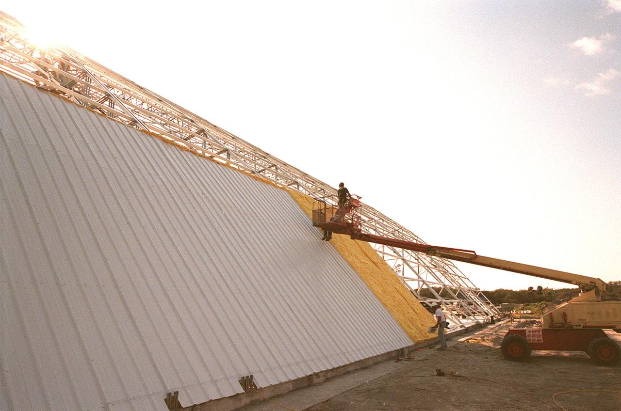 Workers place the first roof panels on the multi-purpose hangar at the site of the $8 million Reusable Launch Vehicle (RLV) Support Complex at Kennedy Space Center. The RLV complex, which includes the hangar and a building for related ground support equipment and administrative/technical support, will be available to accommodate the Space Shuttle; the X-34 RLV technology demonstrator; the L-1011 carrier aircraft for Pegasus and X-34; and other RLV and X-vehicle programs. The complex is jointly funded by the Spaceport Florida Authority, NASA's Space Shuttle Program and KSC. The facility will be operational in early 2000
