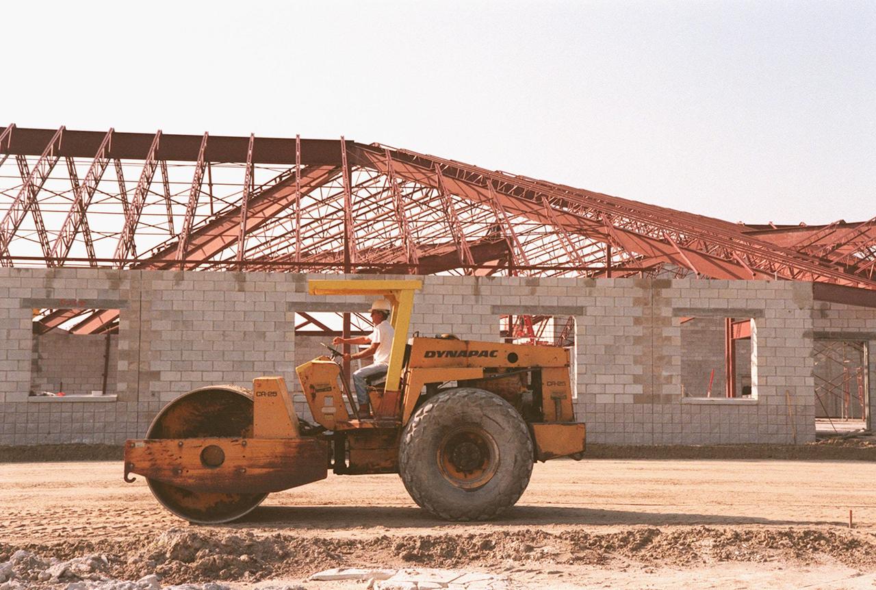 A steam roller packs down the ground next to construction of a support building, part of the $8 million Reusable Launch Vehicle (RLV) Support Complex at Kennedy Space Center. The RLV complex, which includes a multi-purpose hangar and the building to be used for related ground support equipment and administrative/technical support, will be available to accommodate the Space Shuttle; the X-34 RLV technology demonstrator; the L-1011 carrier aircraft for Pegasus and X-34; and other RLV and X-vehicle programs. The complex is jointly funded by the Spaceport Florida Authority, NASA's Space Shuttle Program and KSC. The facility will be operational in early 2000