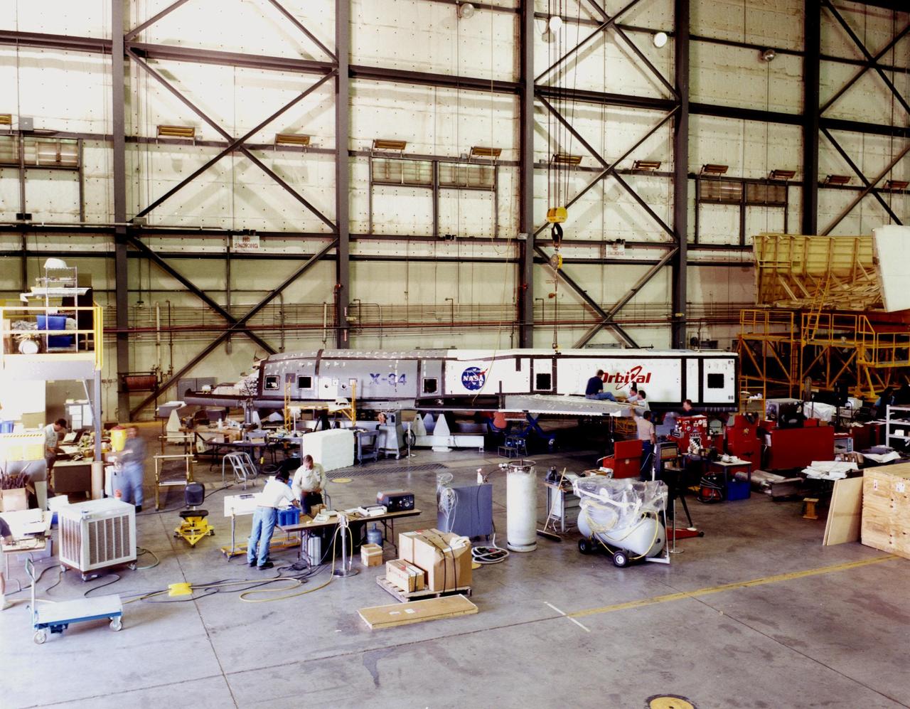 The modified X-34, known as A-1A, rests in the background of the Dryden Flight Research Center at Edwards Air Force Base, Calif., while an integrated team of KSC, Dryden Flight Research Center and Orbital Sciences Corporation engineers and technicians bring the X-34 A-1A vehicle closer to test flight readiness. Since September, eight NASA engineering technicians from KSC's Engineering Prototype Lab have assisted in the complex process of converting the X-34 A-1 vehicle from captive carry status to unpowered flight status, the A-1A. The X-34 is 58.3 feet long, 27.7 feet wide from wing tip to wing tip, and 11.5 feet tall from the bottom of the fuselage to the top of the tail. The autonomously operated technology demonstrator will be air-launched from an L-1011 airplane and should be capable of flying eight times the speed of sound, reaching an altitude of 250,000 feet. The X-34 Project is managed by NASA's Marshall Space Flight Center in Huntsville, Ala