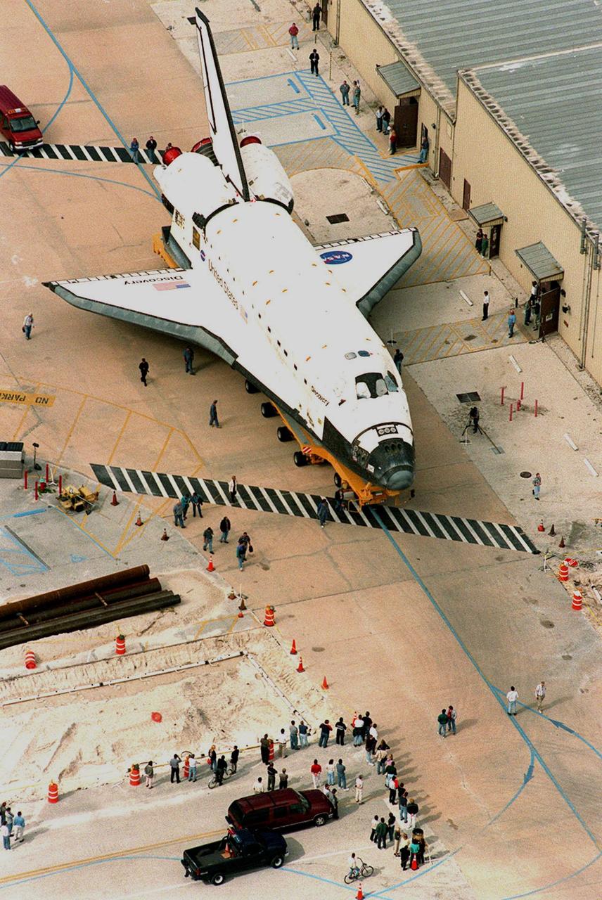 KENNEDY SPACE CENTER, FLA. -- After making a turn in front of the Orbiter Processing Facility (OPF) bay 1, the orbiter Discovery begins moving along the tow-way to the Vehicle Assembly Building as KSC workers watch. At the VAB, Discovery will be mated with an external tank and solid rocket boosters for its launch on mission STS-103. The launch date is currently under review for early December. STS-103, the third Hubble Space Telescope servicing mission, is a "call-up" due to the need to replace portions of the pointing system, the gyros, which have begun to fail on the Hubble Space Telescope. Although Hubble is operating normally and conducting its scientific observations, only three of its six gyroscopes are working properly. The gyroscopes allow the telescope to point at stars, galaxies and planets. The STS-103 crew will also be replacing a Fine Guidance Sensor and an older computer with a new enhanced model, an older data tape recorder with a solid-state digital recorder, a failed spare transmitter with a new one, and degraded insulation on the telescope with new thermal insulation. The crew will also install a Battery Voltage/Temperature Improvement Kit to protect the spacecraft batteries from overcharging and overheating when the telescope goes into a safe mode