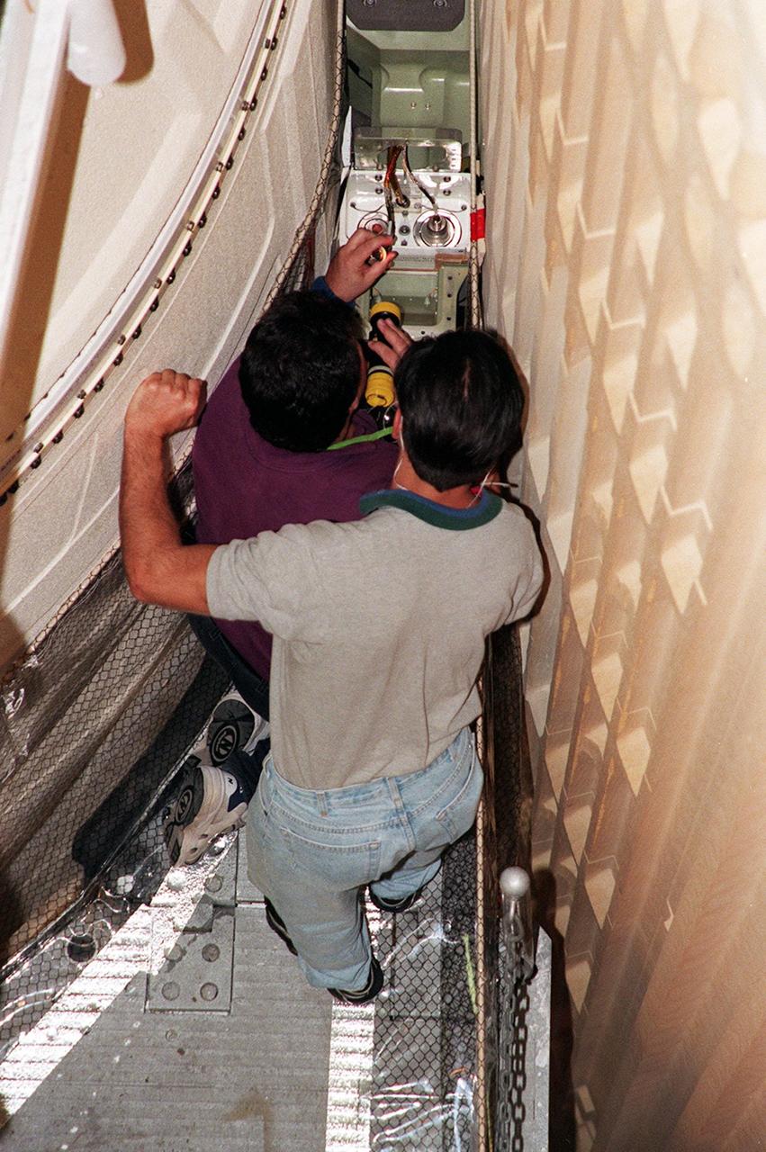 KENNEDY SPACE CENTER, FLA. -- Terry Kent (left), United Space Alliance, and James Silviano (right), NASA, inspect the range safety cable between the external tank and solid rocket boosters (SRB) on Space Shuttle Discovery. The cable, which relays a redundant emergency destruction signal between the SRBs in the unlikely event of a contingency, was damaged during close-out operations and is being replaced. Discovery's processing schedule leads to a target launch date of Dec. 6