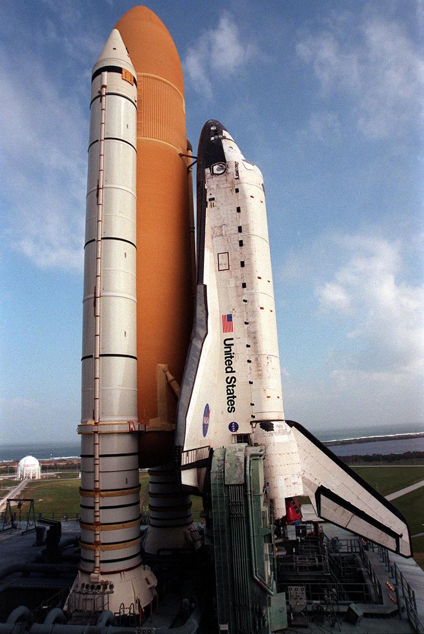 KENNEDY SPACE CENTER, Fla. -- At Launch Pad 39B, Space Shuttle Discovery towers against the hazy blue sky after a seven-hour trek from the Vehicle Assembly Building. The orbiter, external tank and solid rocket boosters will undergo final preparations for the STS-103 launch. The mission is a "call-up" due to the need to replace and repair portions of the Hubble Space Telescope. Although Hubble is operating normally and conducting its scientific observations, only three of its six gyroscopes are working properly. Four EVA's are planned to make the necessary repairs and replacements on the telescope. The STS-103 crew members are Commander Curtis L. Brown Jr., Pilot Scott J. Kelly, Steven L. Smith, C. Michael Foale (Ph.D.), John M. Grunsfeld (Ph.D.), and Claude Nicollier of Switzerland and Jean-François Clervoy of France, both with the European Space Agency. The mission is targeted for launch Dec. 6 at 2:37 a.m. EST
