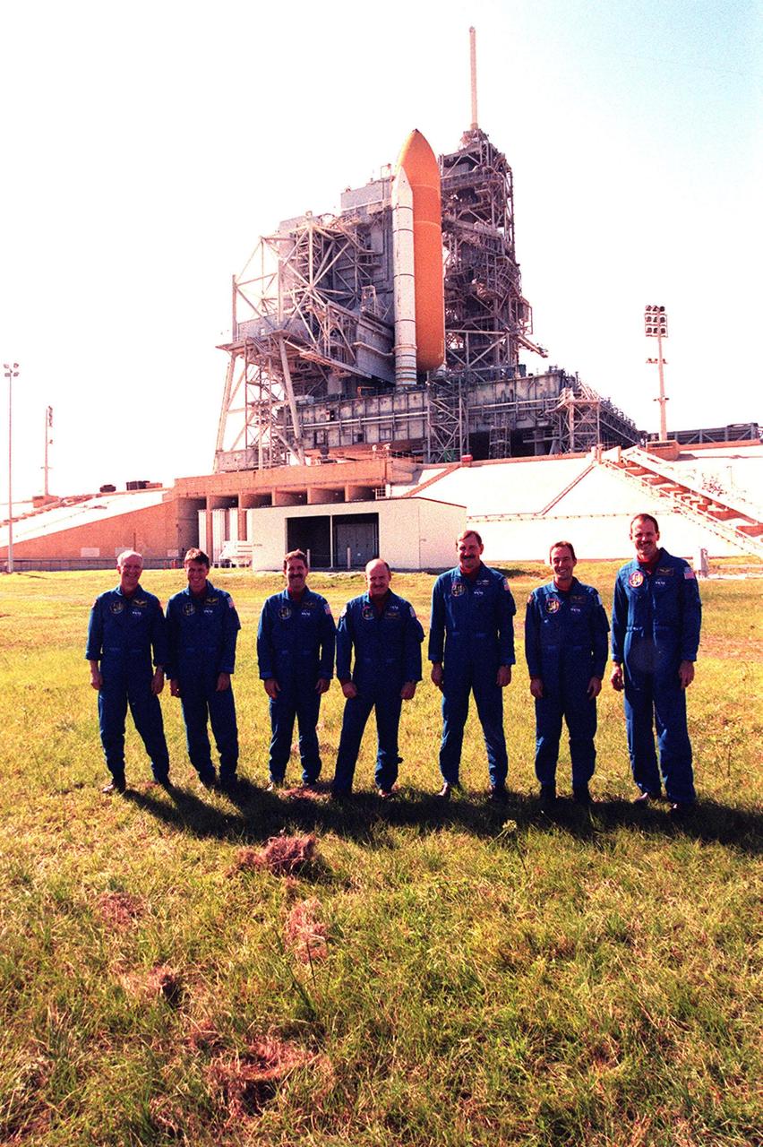 During Terminal Countdown Demonstration Test (TDCT) activities at Launch Pad 39B, the STS-103 crew pose in front of the flame trench, which is situated underneath the Mobile Launcher Platform holding Space Shuttle Discovery. Standing left to right are Mission Specialists Claude Nicollier of Switzerland, who is with the European Space Agency (ESA), C. Michael Foale (Ph.D.), John M. Grunsfeld (Ph.D.), Pilot Scott J. Kelly, Commander Curtis L. Brown Jr., and Mission Specialists Jean-François Clervoy of France, also with ESA, and Steven L. Smith. One of the solid rocket boosters and the external tank that are attached to Discovery can be seen in the photo. The flame trench is made of concrete and refractory brick, and contains an orbiter flame deflector on one side and solid rocket booster flame deflector on the other. The deflectors protect the flame trench floor and pad surface from the intense heat of launch. The TCDT provides the crew with emergency egress training, opportunities to inspect their mission payloads in the orbiter's payload bay, and simulated countdown exercises. STS-103 is a "call-up" mission due to the need to replace and repair portions of the Hubble Space Telescope, including the gyroscopes that allow the telescope to point at stars, galaxies and planets. The STS-103 crew will be replacing a Fine Guidance Sensor, an older computer with a new enhanced model, an older data tape recorder with a solid-state digital recorder, a failed spare transmitter with a new one, and degraded insulation on the telescope with new thermal insulation. The crew will also install a Battery Voltage/Temperature Improvement Kit to protect the spacecraft batteries from overcharging and overheating when the telescope goes into a safe mode. Four EVA's are planned to make the necessary repairs and replacements on the telescope. The mission is targeted for launch Dec. 6 at 2:37 a.m. EST