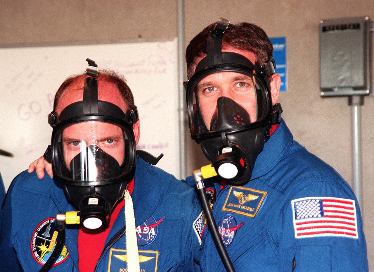 In the bunker at Launch Pad 39B, STS-103 Pilot Scott J. Kelly (left) and Mission Specialist John M. Grunsfeld (Ph.D.) (right) try on oxygen masks during Terminal Countdown Demonstration Test (TCDT) activities. The TCDT provides the crew with emergency egress training, opportunities to inspect their mission payloads in the orbiter's payload bay, and simulated countdown exercises. Other crew members taking part are Commander Curtis L. Brown Jr. and Mission Specialists Steven L. Smith, C. Michael Foale (Ph.D.), and Jean-François Clervoy of France and Claude Nicollier of Switzerland, who are with the European Space Agency. STS-103 is a "call-up" mission due to the need to replace and repair portions of the Hubble Space Telescope, including the gyroscopes that allow the telescope to point at stars, galaxies and planets. The STS-103 crew will be replacing a Fine Guidance Sensor, an older computer with a new enhanced model, an older data tape recorder with a solid-state digital recorder, a failed spare transmitter with a new one, and degraded insulation on the telescope with new thermal insulation. The crew will also install a Battery Voltage/Temperature Improvement Kit to protect the spacecraft batteries from overcharging and overheating when the telescope goes into a safe mode. Four EVA's are planned to make the necessary repairs and replacements on the telescope. The mission is targeted for launch Dec. 6 at 2:37 a.m. EST