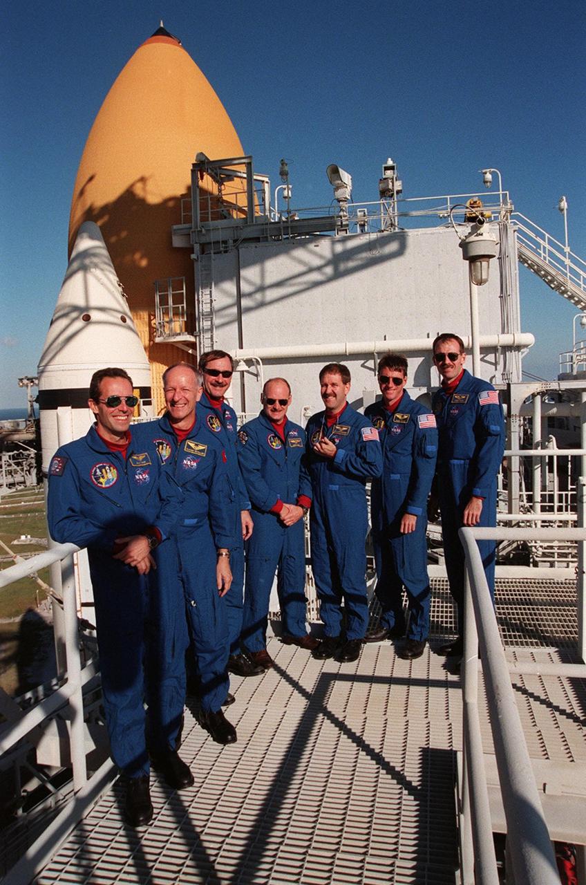 At the 195-foot level of the Fixed Service Structure on Launch Pad 39B, the STS-103 crew take a break from Terminal Countdown Demonstration Test (TCDT) activities. Standing from left to right are Mission Specialists Jean-François Clervoy of France and Claude Nicollier of Switzerland, who are with the European Space Agency; Commander Curtis L. Brown Jr.; Pilot Scott J. Kelly; and Mission Specialists John M. Grunsfeld (Ph.D.), C. Michael Foale (Ph.D.) and Steven L. Smith. The TCDT provides the crew with the emergency egress training, opportunities to inspect their mission payloads in the orbiter's payload bay, and simulated countdown exercises. STS-103 is a "call-up" mission due to the need to replace and repair portions of the Hubble Space Telescope, including the gyroscopes that allow the telescope to point at stars, galaxies and planets. The STS-103 crew will be replacing a Fine Guidance Sensor, an older computer with a new enhanced model, an older data tape recorder with a solid-state digital recorder, a failed spare transmitter with a new one, and degraded insulation on the telescope with new thermal insulation. The crew will also install a Battery Voltage/Temperature Improvement Kit to protect the spacecraft batteries from overcharging and overheating when the telescope goes into a safe mode. Four EVA's are planned to make the necessary repairs and replacements on the telescope. The mission is targeted for launch Dec. 6 at 2:37 a.m. EST