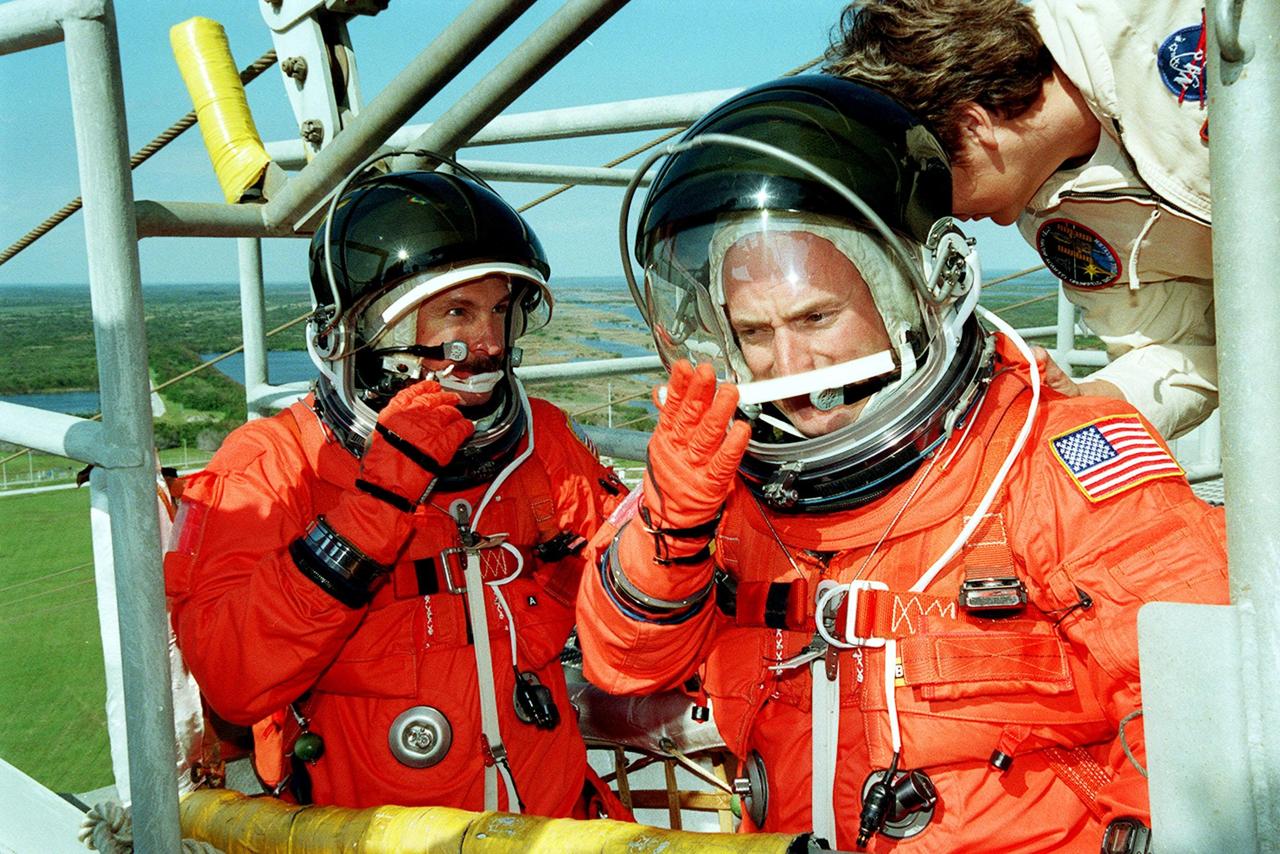 In the slidewire basket on Launch Pad 39B, STS-103 Commander Curtis L. Brown Jr. (left) and Pilot Scott J. Kelly (right) adjust their equipment. The baskets are part of the emergency egress system for persons in the Shuttle vehicle or on the Rotating Service Structure. Seven slidewires extend from the orbiter access arm, with a netted, flatbottom basket suspended from each wire. The other crew members are Mission Specialists Steven L. Smith, C. Michael Foale (Ph.D.), John M. Grunsfeld (Ph.D.), Claude Nicollier of Switzerland, with the European Space Agency (ESA), and Jean-François Clervoy of France, also with ESA.. The STS-103 crew are taking part in Terminal Countdown Demonstration Test (TCDT) activities in preparation for launch. The TCDT provides the crew with the emergency egress training, opportunities to inspect their mission payloads in the orbiter's payload bay, and simulated countdown exercises. STS-103 is a "call-up" mission due to the need to replace and repair portions of the Hubble Space Telescope, including the gyroscopes that allow the telescope to point at stars, galaxies and planets. The STS-103 crew will be replacing a Fine Guidance Sensor, an older computer with a new enhanced model, an older data tape recorder with a solid-state digital recorder, a failed spare transmitter with a new one, and degraded insulation on the telescope with new thermal insulation. The crew will also install a Battery Voltage/Temperature Improvement Kit to protect the spacecraft batteries from overcharging and overheating when the telescope goes into a safe mode. Four EVA's are planned to make the necessary repairs and replacements on the telescope. The mission is targeted for launch Dec. 6 at 2:37 a.m. EST