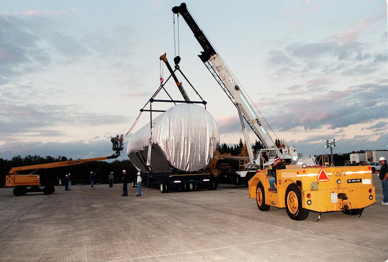 KENNEDY SPACE CENTER, FLA. -- In the waning afternoon light, cranes secure the P3 truss on the transporter while a tractor and driver wait to move it to the Operations and Checkout Building. The second port-side truss is a segment of the International Space Station (ISS), scheduled to be added to the ISS on mission STS-115 in 2002 aboard Space Shuttle Atlantis. P3 will be attached to the first port truss segment (P1).
