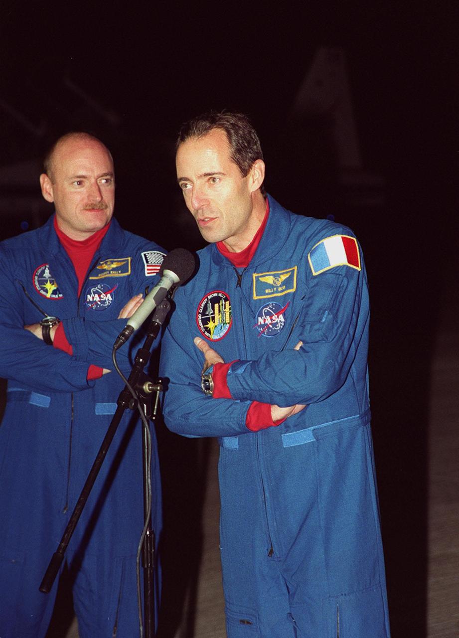 STS-103 Mission Specialist Jean-François Clervoy of France (at microphone) greets the media at the Shuttle Landing Facility as Pilot Scott J. Kelly looks on. The crew arrived at KSC aboard T-38 jets to make final preparations for their launch. The other STS-103 crew members are Commander Curtis L. Brown Jr. and Mission Specialists Steven L. Smith, C. Michael Foale (Ph.D.), John M. Grunsfeld (Ph.D.), and Claude Nicollier of Switzerland. Nicollier and Clervoy are with the European Space Agency. The mission, to service the Hubble Space Telescope a third time, is scheduled for launch Dec. 11 at 12:13 a.m. EST from Launch Pad 39B