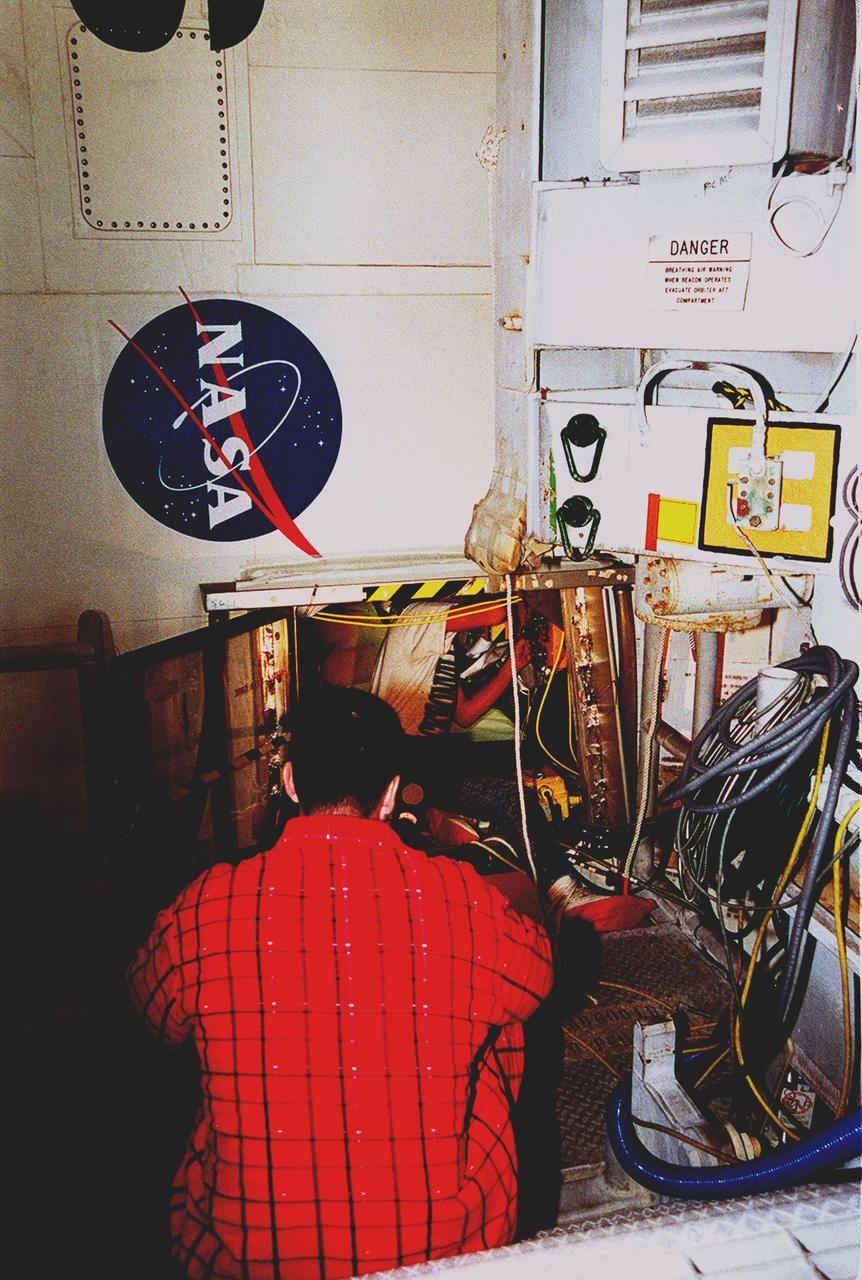 KENNEDY SPACE CENTER, FLA. -- Chris Kidd, with United Space Alliance (USA) stands by outside the aft compartment of Discovery while Todd Biddle (USA) inspects wiring inside. Electrical wire inspections and repairs in the orbiter's payload bay, external tank umbilical and engine compartment have been ongoing for more than a month and are near completion. Launch of Space Shuttle Discovery on mission STS-103 is scheduled for Dec. 11 at 11:42 p.m. from Launch Pad 39B. STS-103 is the third servicing mission for the Hubble Space Telescope