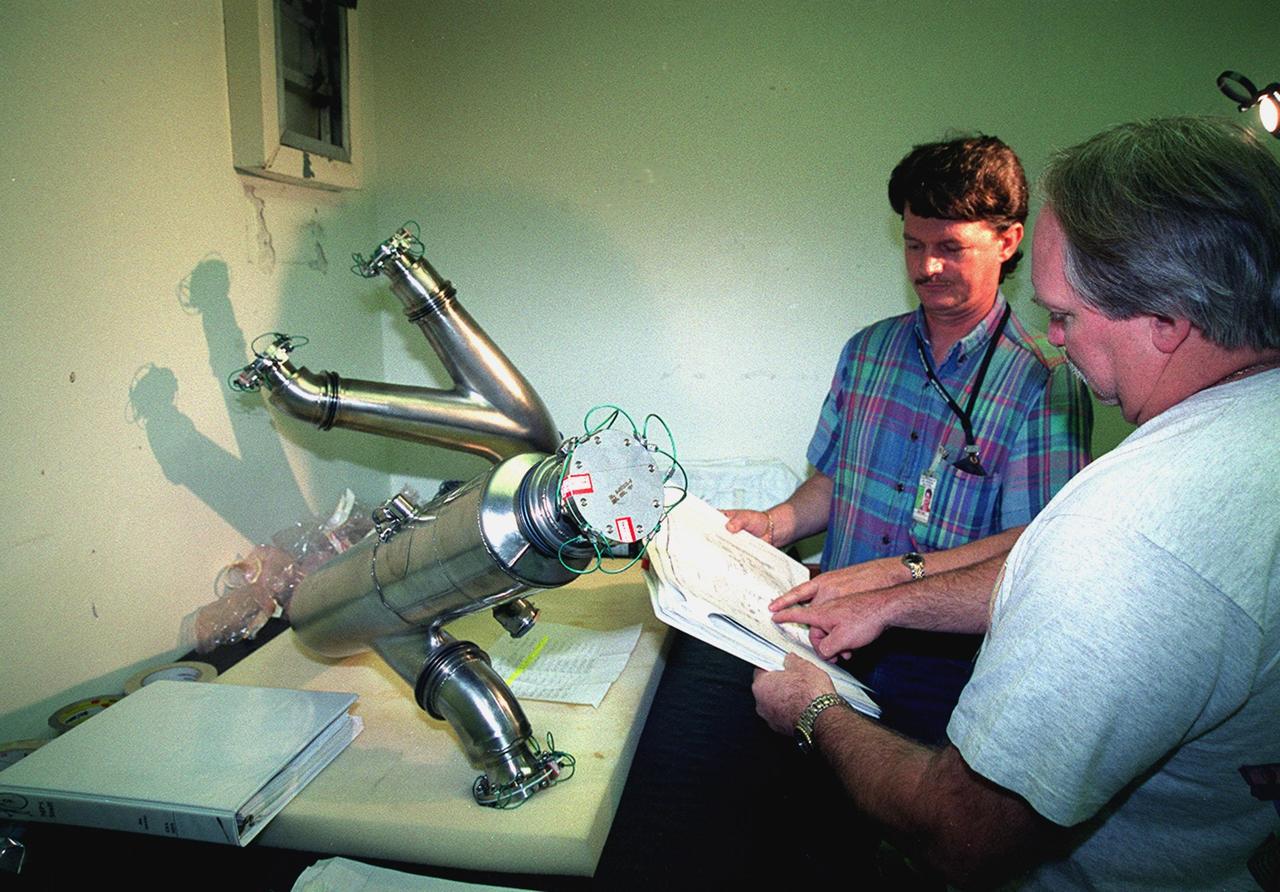 James Stickley (left) and Derry Dilby (right), who are with United Space Alliance, check over a spare four-inch diameter LH2 recirculation line that will be used to replace a damaged LH2 line in the orbiter Discovery. The line recirculates hydrogen from the Shuttle main engines back to the external tank during prelaunch engine conditioning. Workers noted a dent in the line during routine aft compartment inspections Tuesday, Dec. 7. The dent measures 12 inches long and about ½-inch deep. Managers expect the replacement work to take about 3 days, followed by system retests and final aft compartment close-outs. Preliminary assessments reflect a launch date of Space Shuttle Discovery on mission STS-103 no earlier than Dec. 16. STS-103 is the third servicing mission for the Hubble Space Telescope