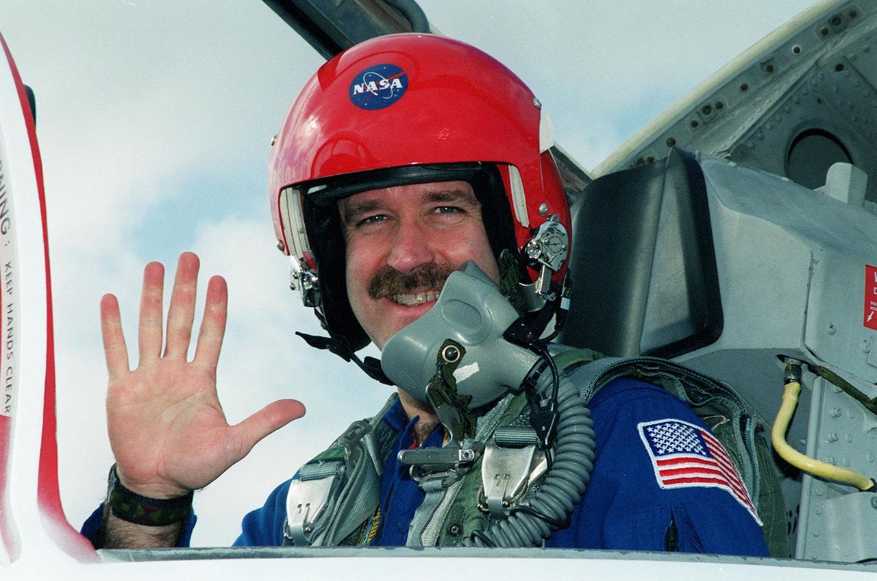 STS-103 Mission Specialist John M. Grunsfeld (Ph.D.) waves from the rear seat of a T-38 training jet before beginning practice flights. He joins other crew members Commander Curtis L. Brown Jr., Pilot Scott J. Kelly and Mission Specialists Steven L. Smith, C. Michael Foale (Ph.D.), Claude Nicollier of Switzerland and Jean-François Clervoy of France, for pre-launch preparations on mission STS-103 aboard Space Shuttle Discovery. Nicollier and Clervoy are with the European Space Agency. The mission, to service the Hubble Space Telescope, is scheduled for launch Dec. 16 at 9:18 p.m. EST from Launch Pad 39B. The mission is expected to last about 9 days and 21 hours. Discovery is expected to land at KSC Sunday, Dec. 26, at 6:56 p.m. EST