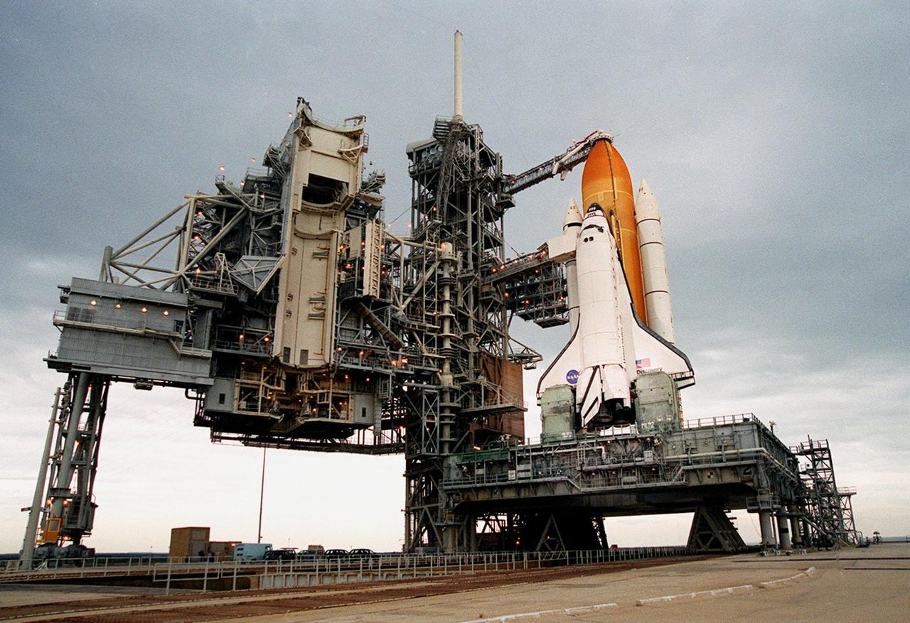 After rollback of the Rotating Service Structure at Launch Pad 39B (left) before dawn, the Space Shuttle Discovery is revealed poised for flight on mission STS-103. The rollback of the structure was complete at 4:46 a.m. EST. STS-103 is scheduled for launch Dec. 16 at 9:18 p.m. EST. The mission is expected to last about 9 days and 21 hours with a landing at KSC Sunday, Dec. 26, at 6:56 p.m. EST