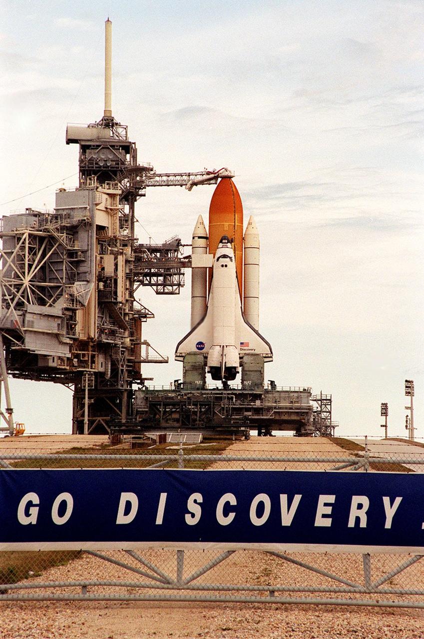 A cloud-streaked sky provides backdrop for Space Shuttle Discovery as it waits for liftoff on mission STS-103 from Launch Pad 39B. The tower at its left is the Fixed Service Structure, topped by the 80-foot-tall fiberglass mast that helps provide protection from lightning strikes. Below it, extending outward, is the external tank gaseous oxygen vent arm system with the vent hood (commonly called the "beanie cap") poised above the external tank. The retractable arm and the beanie cap are designed to vent gaseous oxygen vapors away from the Space Shuttle. The arm truss section is 65 feet long and the diameter of the vent hood is 13 feet. Extending toward the cabin of the orbiter below is the orbiter access arm, with the environmental chamber (called the White Room) at the end. Through this chamber the crew enters the orbiter. The STS-103 mission, to service the Hubble Space Telescope, is scheduled for launch Dec. 17 at 8:47 p.m. EST. Mission objectives include replacing gyroscopes and an old computer, installing another solid state recorder, and replacing damaged insulation in the telescope. The mission is expected to last about 8 days and 21 hours. Discovery is expected to land at KSC Sunday, Dec. 26, at about 6:25 p.m. EST