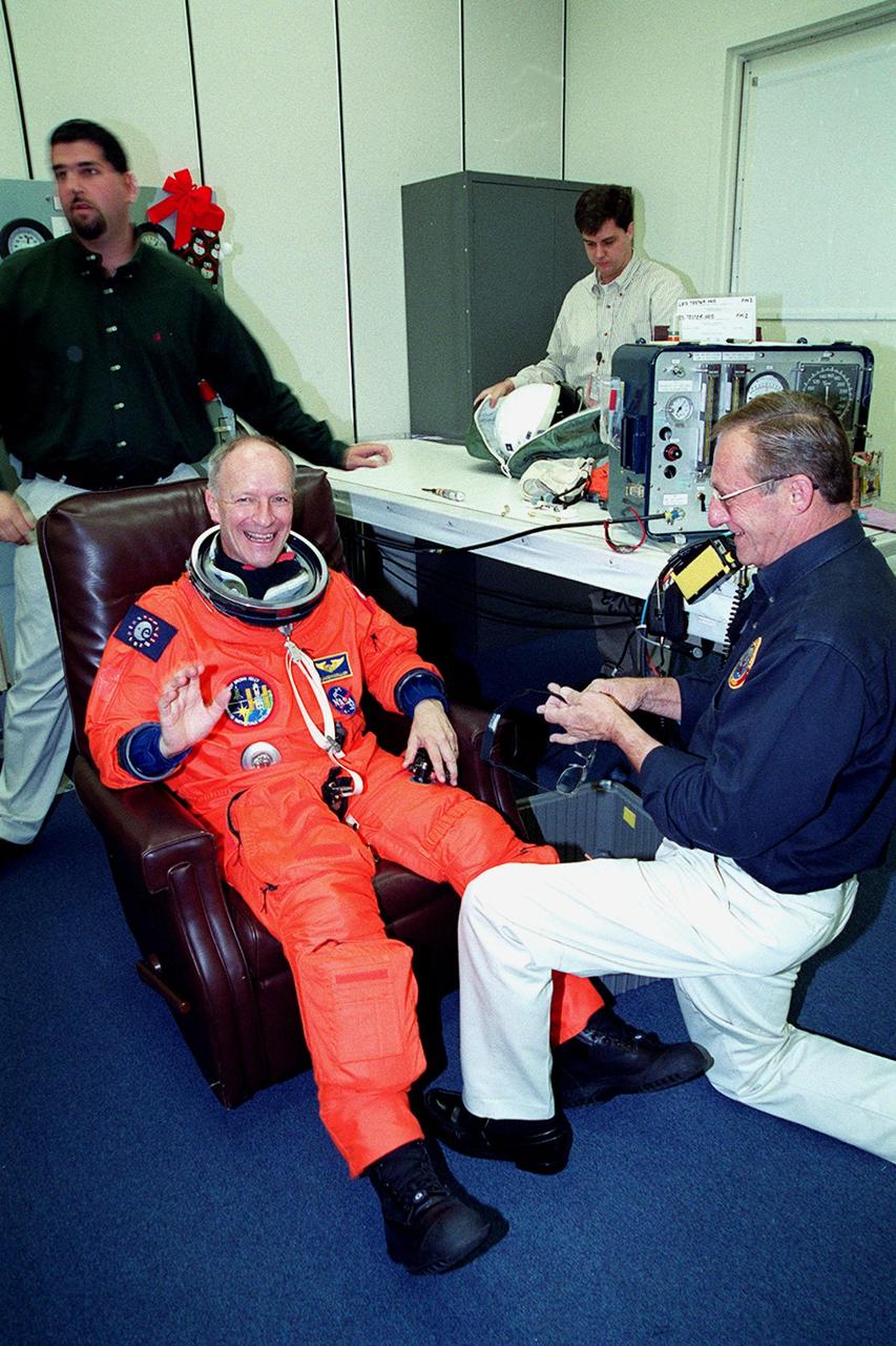 In the Operations and Checkout Building, STS-103 Mission Specialist Claude Nicollier of Switzerland waves while having his launch and entry suit checked by a suit techician during final launch preparations. Other crew members are Commander Curtis L. Brown Jr., Pilot Scott J. Kelly and Mission Specialists Steven L. Smith, C. Michael Foale (Ph.D.), John M. Grunsfeld (Ph.D.) and Jean-François Clervoy of France. Nicollier and Clervoy are with the European Space Agency. The STS-103 mission, to service the Hubble Space Telescope, is scheduled for launch Dec. 17 at 8:47 p.m. EST from Launch Pad 39B. Mission objectives include replacing gyroscopes and an old computer, installing another solid state recorder, and replacing damaged insulation in the telescope. After the 8-day, 21-hour mission, Discovery is expected to land at KSC Sunday, Dec. 26, at about 6:30 p.m. EST