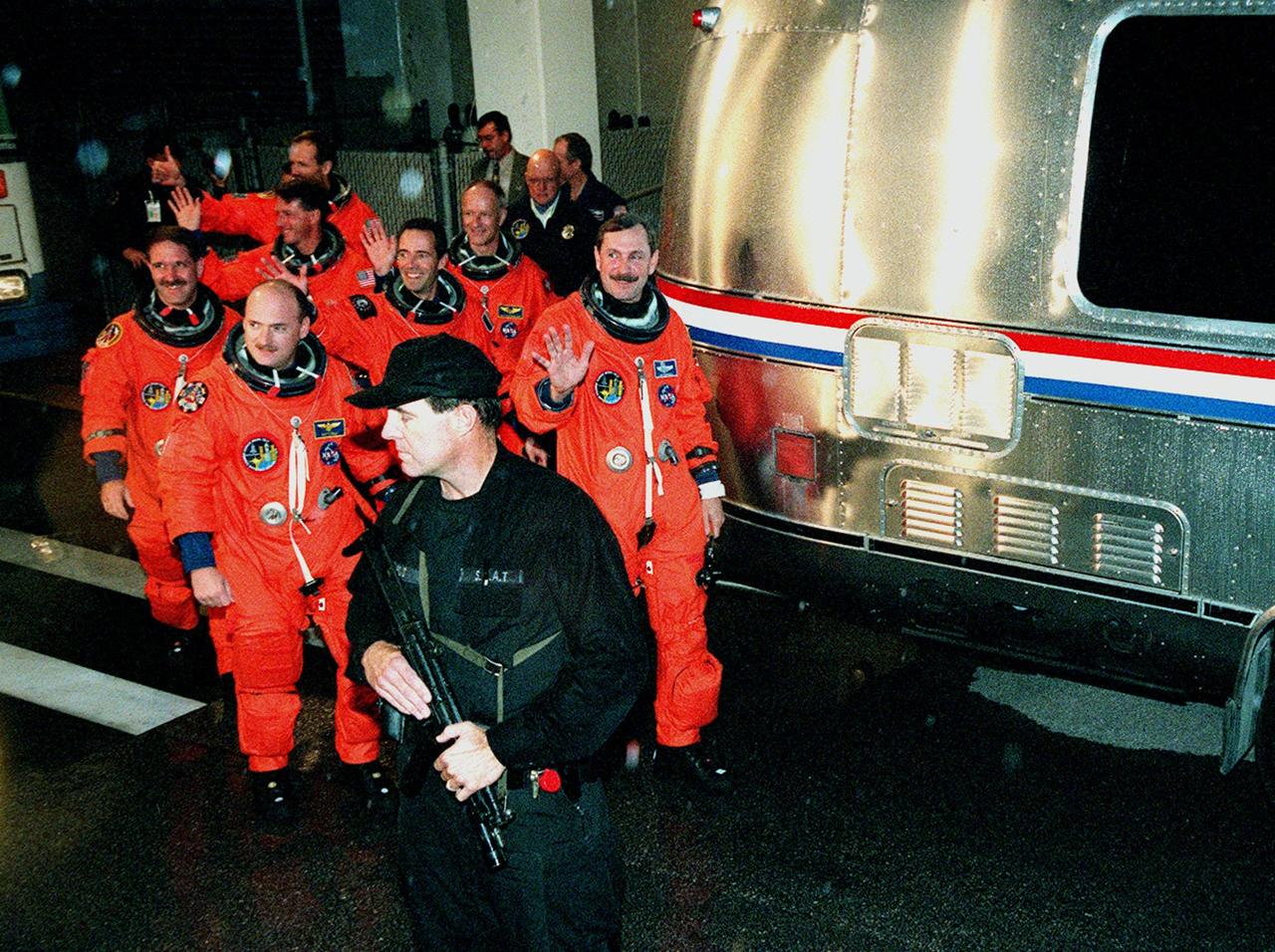 The STS-103 crew smile and wave to onlookers as they head toward the "Astrovan" at right that will carry them to Launch Pad 39B for liftoff of Space Shuttle Discovery. In their orange launch and entry suits, they are (front row) Pilot Scott J. Kelly and Commander Curtis L. Brown Jr., (second row) Mission Specialists John M. Grunsfeld (Ph.D.) and Jean-Francois Clervoy of France, (third row) C. Michael Foale (Ph. D.) and Claude Nicollier of Switzerland, and bringing up the rear, Steven L. Smith. The STS-103 mission, to service the Hubble Space Telescope, is scheduled for launch Dec. 17 at 8:47 p.m. EST from Launch Pad 39B. Mission objectives include replacing gyroscopes and an old computer, installing another solid state recorder, and replacing damaged insulation in the telescope. After the 8-day, 21-hour mission, Discovery is expected to land at KSC Sunday, Dec. 26, at about 6:30 p.m. EST