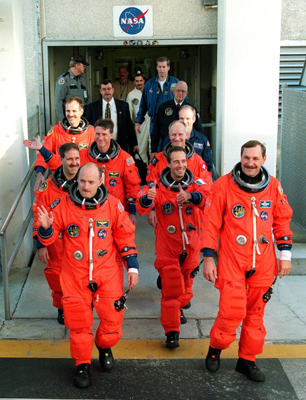 The STS-103 crew in their launch and entry suits signal confidence as they head out of the Operations and Checkout Building, for the second time in two days, on their way to Launch Pad 39B and liftoff of Space Shuttle Discovery. From front to back by two's are Pilot Scott J. Kelly and Commander Curtis L. Brown Jr., Mission Specialists John M. Grunsfeld (Ph.D.) and Jean-Francois Clervoy of France, C. Michael Foale (Ph.D.) and Claude Nicollier of Switzerland, and Steven L. Smith taking up the rear. The previous launch attempt on Dec. 17 was scrubbed about 8:52 p.m. due to numerous violations of weather launch commit criteria at KSC. The mission, to service the Hubble Space Telescope, is now scheduled for launch Dec. 19 at 7:50 p.m. EST from Launch Pad 39B. Mission objectives include replacing gyroscopes and an old computer, installing another solid state recorder, and replacing damaged insulation in the telescope. After the 7-day, 21-hour mission, Discovery is expected to land at KSC Monday, Dec. 27, at about 5:24 p.m. EST