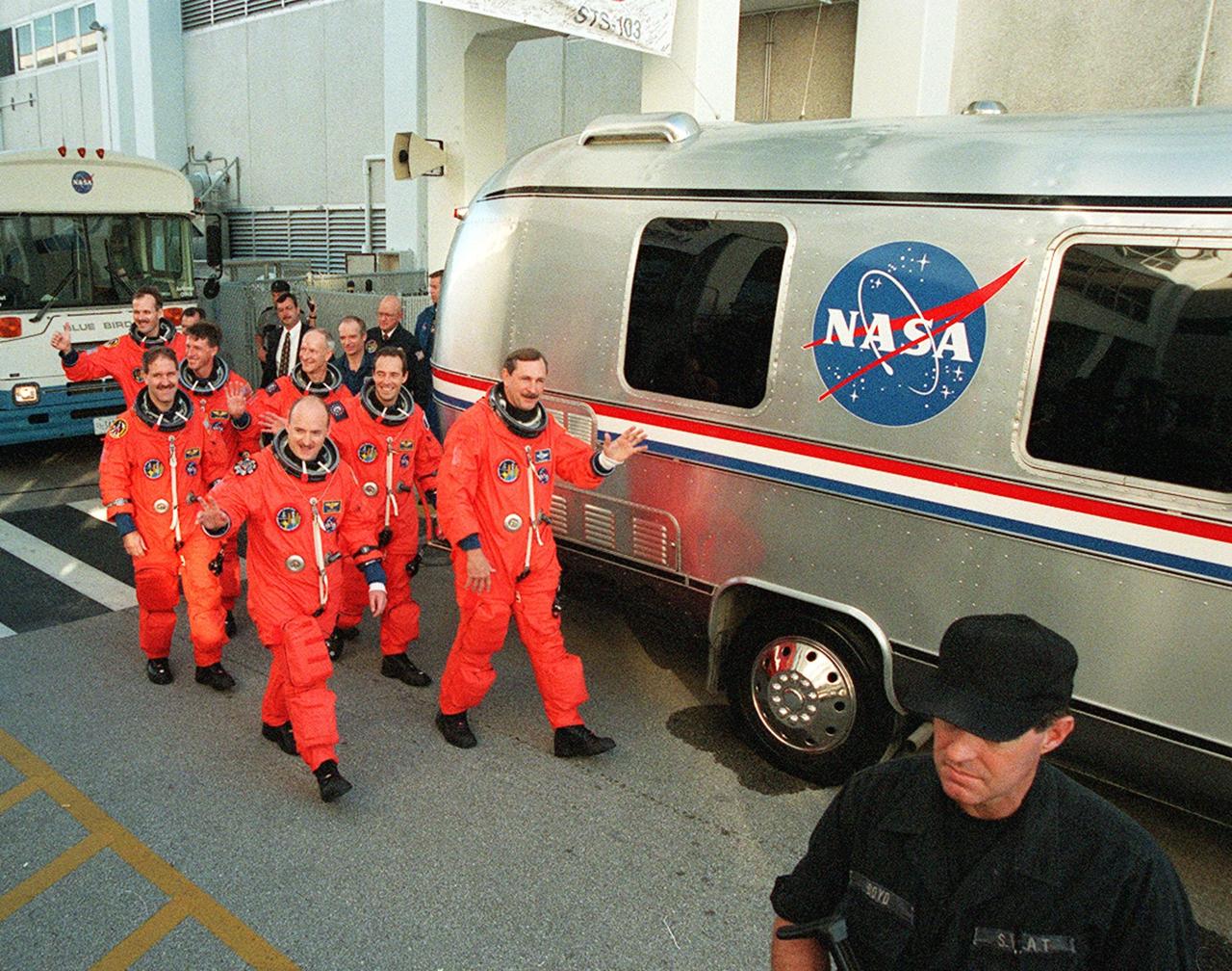 An eager STS-103 crew emerge from behind the "Astrovan" at the Operations and Checkout Building to board the vehicle for transfer to Launch Pad 39B. Walking in pairs (from front to back) are Pilot Scott J. Kelly and Commander Curtis L. Brown Jr., Mission Specialists John M. Grunsfeld (Ph.D.) and Jean-Francois Clervoy of France, C. Michael Foale (Ph.D.) and Claude Nicollier of Switzerland, and Steven L. Smith taking up the rear. A previous launch attempt on Dec. 17 was scrubbed about 8:52 p.m. due to numerous violations of weather launch commit criteria at KSC. The mission, to service the Hubble Space Telescope, is now scheduled for launch Dec. 19 at 7:50 p.m. EST from Launch Pad 39B. Mission objectives include replacing gyroscopes and an old computer, installing another solid state recorder, and replacing damaged insulation in the telescope. After the 7-day, 21-hour mission, Discovery is expected to land at KSC Monday, Dec. 27, at about 5:24 p.m. EST