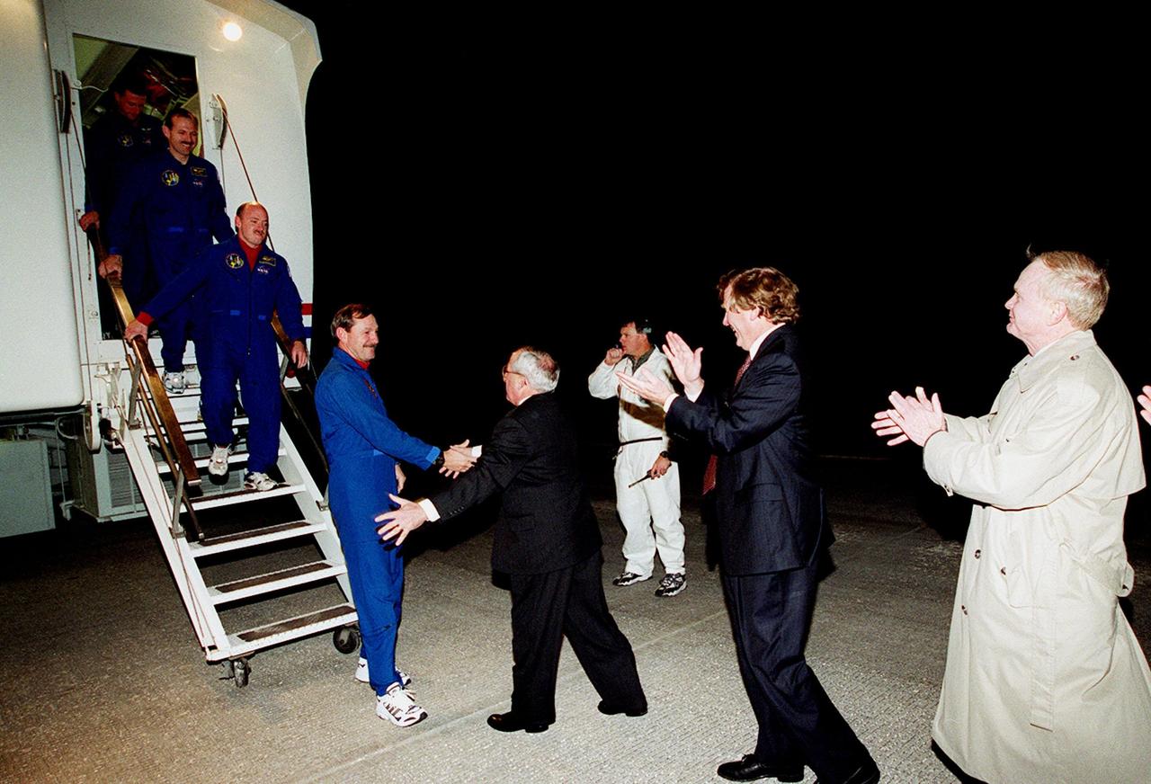 As he exits the Crew Hatch Access Vehicle, STS-103 Commander Curtis L. Brown Jr. is greeted with a handshake by Joseph Rothenberg, associate administrator, Office of Space Flight. Descending the stairs behind Brown are (left to right) Mission Specialists C. Michael Foale (Ph.D.) and John M. Grunsfeld (Ph.D.) and Pilot Scott J. Kelly. At right, applauding the astronauts return are Earle Huckins, deputy associate administrator, Office of Space Science, and Roy Bridges, director, Kennedy Space Center. Others in the crew (not shown) are Mission Specialists Steven L. Smith, and Jean-Francois Clervoy of France and Claude Nicollier of Switzerland, who are with the European Space Agency. The crew of seven completed a successful eight-day mission to service the Hubble Space Telescope, spending the Christmas holiday in space in order to accomplish their mission before the end of 1999. During the mission, Discovery's four space-walking astronauts, Smith, Foale, Grunsfeld and Nicollier, spent 24 hours and 33 minutes upgrading and refurbishing Hubble, making it more capable than ever to renew its observations of the universe. Mission objectives included replacing gyroscopes and an old computer, installing another solid state recorder, and replacing damaged insulation in the telescope. Hubble was released from the end of Discovery's robot arm on Christmas Day. Main gear touchdown was at 7:00:47 p.m. EST. Nose gear touchdown occurred at 7:00:58 p.m. EST and wheel stop at 7:01:34 p.m. EST. This was the 96th flight in the Space Shuttle program and the 27th for the orbiter Discovery. The landing was the 20th consecutive Shuttle landing in Florida and the 13th night landing in Shuttle program history