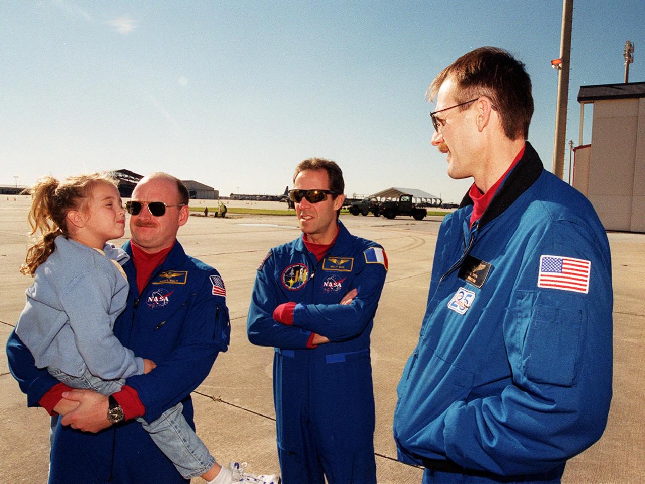 STS-103 Pilot Scott J. Kelly holds his daughter as he talks to Mission Specialists and fellow crew members Jean-François Clervoy of France and Steven L. Smith on the runway at Patrick Air Force Base. The STS-103 crew and their families are preparing to board an airplane that will return them to their home base at the Johnson Space Center in Houston following the successful completion of their mission. Discovery landed in darkness the previous evening, Dec. 27, on runway 33 at KSC's Shuttle Landing Facility at 7:00:47 p.m. EST. This was the first time that a Shuttle crew spent the Christmas holiday in space. The other STS-103 crew members are Commander Curtis L. Brown Jr. and Mission Specialists C. Michael Foale (Ph.D.), John M. Grunsfeld (Ph.D.), and Claude Nicollier of Switzerland. The STS-103 mission supplied the Hubble Space Telescope with six new gyroscopes, six new voltage/temperature improvement kits, a new onboard computer, a new solid state recorder and new data transmitter, and a new fine guidance sensor along with new insulation on parts of the orbiting telescope. This was the 96th flight in the Space Shuttle program and the 27th for the orbiter Discovery