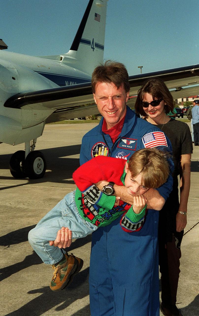 STS-103 Mission Specialist C. Michael Foale (Ph.D.) holds one of his children on the runway at Patrick Air Force Base, as his wife, Rhonda, looks on. The STS-103 crew and their families are preparing to board an airplane that will return them to their home base at the Johnson Space Center in Houston following the successful completion of their mission. Discovery landed in darkness the previous evening, Dec. 27, on runway 33 at KSC's Shuttle Landing Facility at 7:00:47 p.m. EST. This was the first time that a Shuttle crew spent the Christmas holiday in space. The other STS-103 crew members are Commander Curtis L. Brown Jr.; Pilot Scott J. Kelly; and Mission Specialists Steven L. Smith, John M. Grunsfeld (Ph.D.), Claude Nicollier of Switzerland and Jean-François Clervoy of France. The STS-103 mission supplied the Hubble Space Telescope with six new gyroscopes, six new voltage/temperature improvement kits, a new onboard computer, a new solid state recorder and new data transmitter, and a new fine guidance sensor along with new insulation on parts of the orbiting telescope. This was the 96th flight in the Space Shuttle program and the 27th for the orbiter Discovery