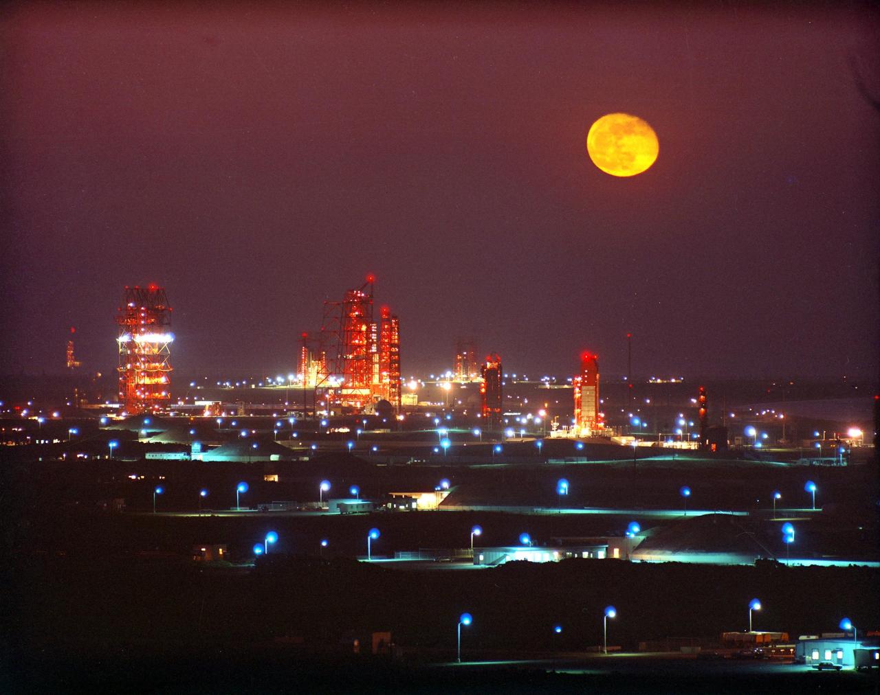 KENNEDY SPACE CENTER, FLA. -- A full moon is outdazzled by the liglhts of the gantries below on "Missile Row" as they stretch north along the shoreline of Cape Canaveral Air Force Station.