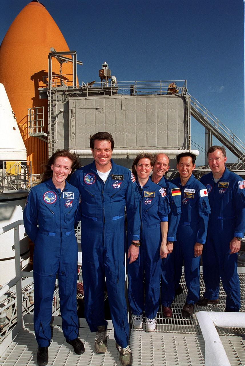 KENNEDY SPACE CENTER, Fla. --  At the 167-foot level of the Fixed Service Structure on Launch Pad 39A, the STS-99 crew pose for a photograph during Terminal Countdown Demonstration Test (TCDT) activities. Standing left to right are Mission Specialist Janet Lynn Kavandi (Ph.D.), Commander Kevin Kregel, Mission Specialists Janice Voss (Ph.D.), Gerhard Thiele and Mamoru Mohri, and Pilot Dominic Gorie. Thiele is with the European Space Agency and Mohri is with the National Space Development Agency (NASDA) of Japan. Behind them (left) are visible the top of a solid rocket booster (white) and external tank (orange). The TCDT provides the crew with simulated countdown exercises, emergency egress training, and opportunities to inspect the mission payloads in the orbiter's payload bay. STS-99 is the Shuttle Radar Topography Mission, which will chart a new course, using two antennae and a 200-foot-long section of space station-derived mast protruding from the payload bay to produce unrivaled 3-D images of the Earth's surface. The result of the Shuttle Radar Topography Mission could be close to 1 trillion measurements of the Earth's topography. Besides contributing to the production of better maps, these measurements could lead to improved water drainage modeling, more realistic flight simulators, better locations for cell phone towers, and enhanced navigation safety. Launch of Endeavour on the 11-day mission is scheduled for Jan. 31 at 12:47 p.m. EST