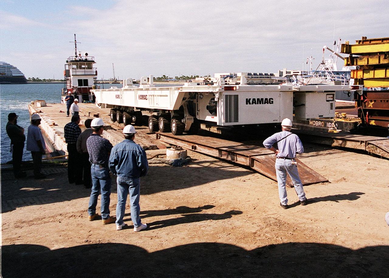 The first of two new payload transporters for Kennedy Space Center arrives at Port Canaveral. They were shipped by barge from their manufacturer, the KAMAG Company of Ulm, Germany. The transporters are used to carry spacecraft and International Space Station elements from payload facilities to and from the launch pads and orbiter hangars. Each transporter is 65 feet long and 22 feet wide and has 24 tires divided between its two axles. The transporter travels 10 miles per hour unloaded, 5 miles per hour when loaded; it weighs up to 172,000 pounds when the canister with payloads rides atop. The transporters will be outfitted with four subsystems for monitoring the environment inside the canister during the payload moves: the Electrical Power System, Environmental Control System, Instrumentation and Communications System, and the Fluids and Gases System. Engineers and technicians are being trained on the transporter's operation and maintenance. The new transporters are replacing the 20-year-old existing Payload Canister Transporter system