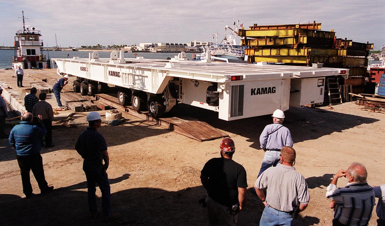 One of two new payload transporters for Kennedy Space Center arrives at Port Canaveral. They were shipped by barge from their manufacturer, the KAMAG Company of Ulm, Germany. The transporters are used to carry spacecraft and International Space Station elements from payload facilities to and from the launch pads and orbiter hangars. Each transporter is 65 feet long and 22 feet wide and has 24 tires divided between its two axles. The transporter travels 10 miles per hour unloaded, 5 miles per hour when loaded; it weighs up to 172,000 pounds when the canister with payloads rides atop. The transporters will be outfitted with four subsystems for monitoring the environment inside the canister during the payload moves: the Electrical Power System, Environmental Control System, Instrumentation and Communications System, and the Fluids and Gases System. Engineers and technicians are being trained on the transporter's operation and maintenance. The new transporters are replacing the 20-year-old existing Payload Canister Transporter system