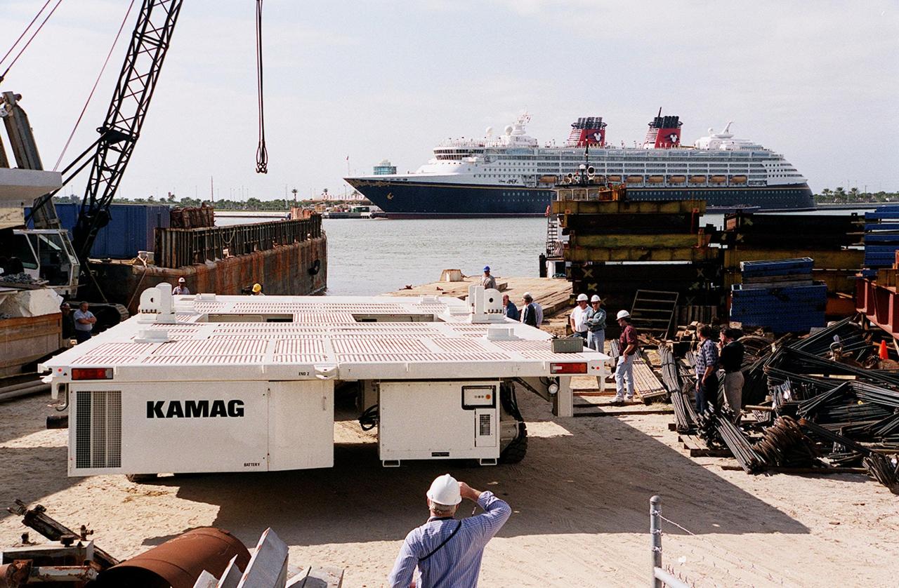 One of two new payload transporters for Kennedy Space Center arrives at Port Canaveral. In the background is a cruise ship docked at the Port. The transporters were shipped by barge from their manufacturer, the KAMAG Company of Ulm, Germany. They are used to carry spacecraft and International Space Station elements from payload facilities to and from the launch pads and orbiter hangars. Each transporter is 65 feet long and 22 feet wide and has 24 tires divided between its two axles. The transporter travels 10 miles per hour unloaded, 5 miles per hour when loaded; it weighs up to 172,000 pounds when the canister with payloads rides atop. The transporters will be outfitted with four subsystems for monitoring the environment inside the canister during the payload moves: the Electrical Power System, Environmental Control System, Instrumentation and Communications System, and the Fluids and Gases System. Engineers and technicians are being trained on the transporter's operation and maintenance. The new transporters are replacing the 20-year-old existing Payload Canister Transporter system