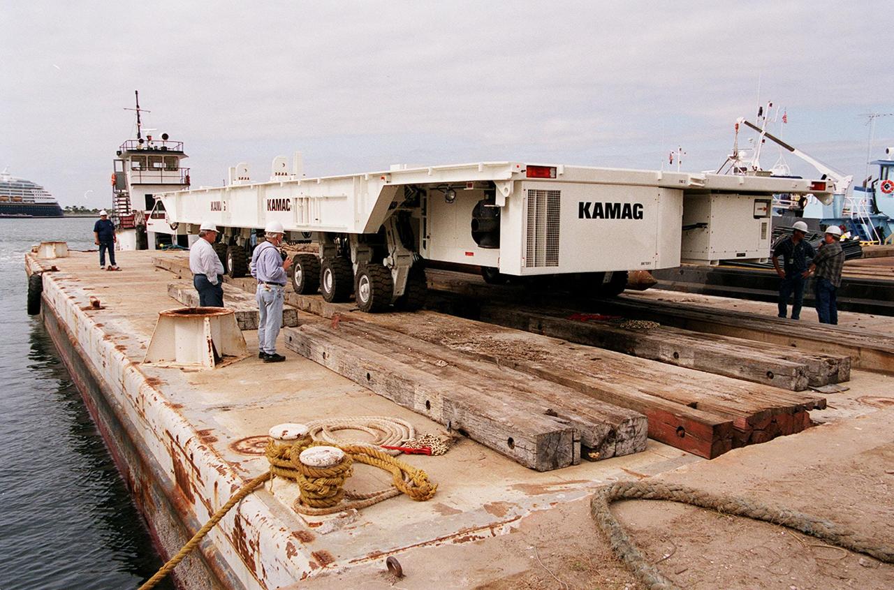 One of two new payload transporters for Kennedy Space Center sits on the dock at Port Canaveral. In the background is a cruise ship docked at the Port. The transporters were shipped by barge from their manufacturer, the KAMAG Company of Ulm, Germany. They are used to carry spacecraft and International Space Station elements from payload facilities to and from the launch pads and orbiter hangars. Each transporter is 65 feet long and 22 feet wide and has 24 tires divided between its two axles. The transporter travels 10 miles per hour unloaded, 5 miles per hour when loaded; it weighs up to 172,000 pounds when the canister with payloads rides atop. The transporters will be outfitted with four subsystems for monitoring the environment inside the canister during the payload moves: the Electrical Power System, Environmental Control System, Instrumentation and Communications System, and the Fluids and Gases System. Engineers and technicians are being trained on the transporter's operation and maintenance. The new transporters are replacing the 20-year-old existing Payload Canister Transporter system