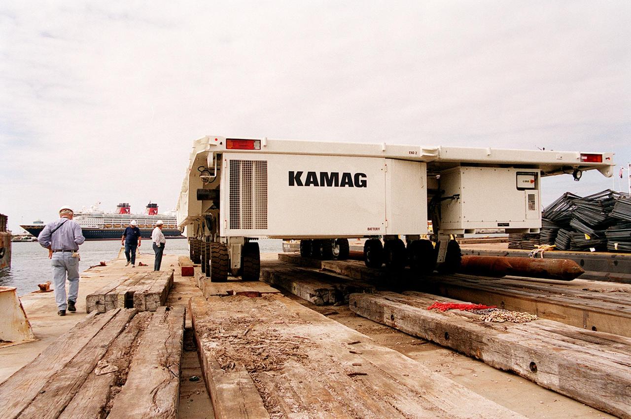 One of two new payload transporters for Kennedy Space Center sits on the dock at Port Canaveral. In the background is a cruise ship docked at the Port. The transporters were shipped by barge from their manufacturer, the KAMAG Company of Ulm, Germany. They are used to carry spacecraft and International Space Station elements from payload facilities to and from the launch pads and orbiter hangars. Each transporter is 65 feet long and 22 feet wide and has 24 tires divided between its two axles. The transporter travels 10 miles per hour unloaded, 5 miles per hour when loaded; it weighs up to 172,000 pounds when the canister with payloads rides atop. The transporters will be outfitted with four subsystems for monitoring the environment inside the canister during the payload moves: the Electrical Power System, Environmental Control System, Instrumentation and Communications System, and the Fluids and Gases System. Engineers and technicians are being trained on the transporter's operation and maintenance. The new transporters are replacing the 20-year-old existing Payload Canister Transporter system