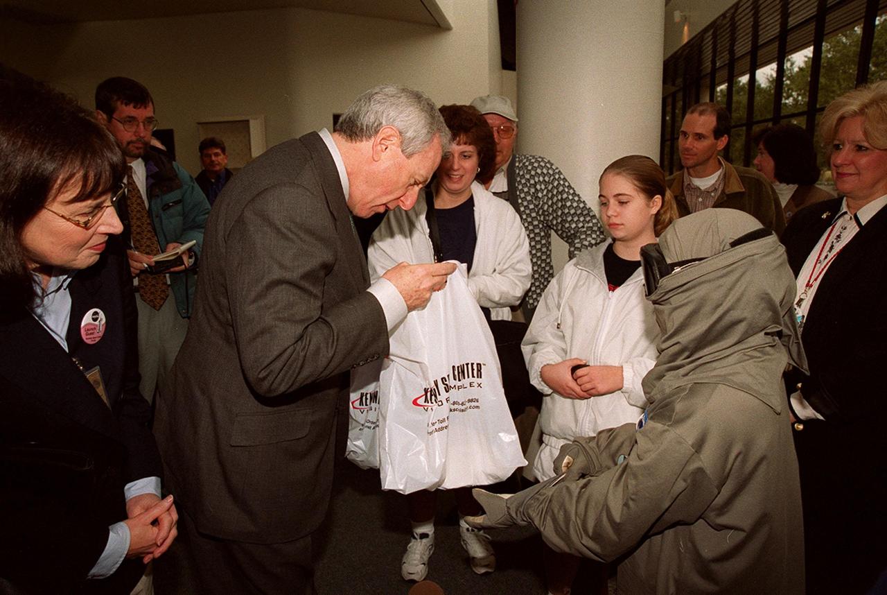 NASA Administrator Dan Goldin (center) presents a bag of special gifts to 10-year-old Jonathan Pierce (right), who is garbed in a protective cooling suit designed by NASA. In the background, between them, are Jonathan's mother, Penny; his grandfather, John Janocka; and his sister, Jaimie.. At left is Mrs. Goldin. Jonathan suffers from erythropoietic protoporphyria, a rare condition that makes his body unable to withstand ultraviolet rays. The suit allows him to be outside during the day, which would otherwise be impossible. Jonathan's trip was funded by the Make-A-Wish Foundation and included a visit to Disney World. He and his family were among a dozen VIPs at KSC to view the launch of STS-99